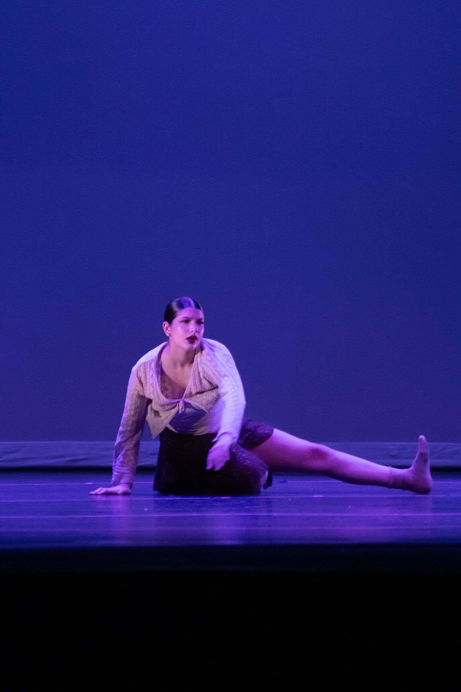 A dancer in white sits on a blue-lit stage in a dramatic pose.