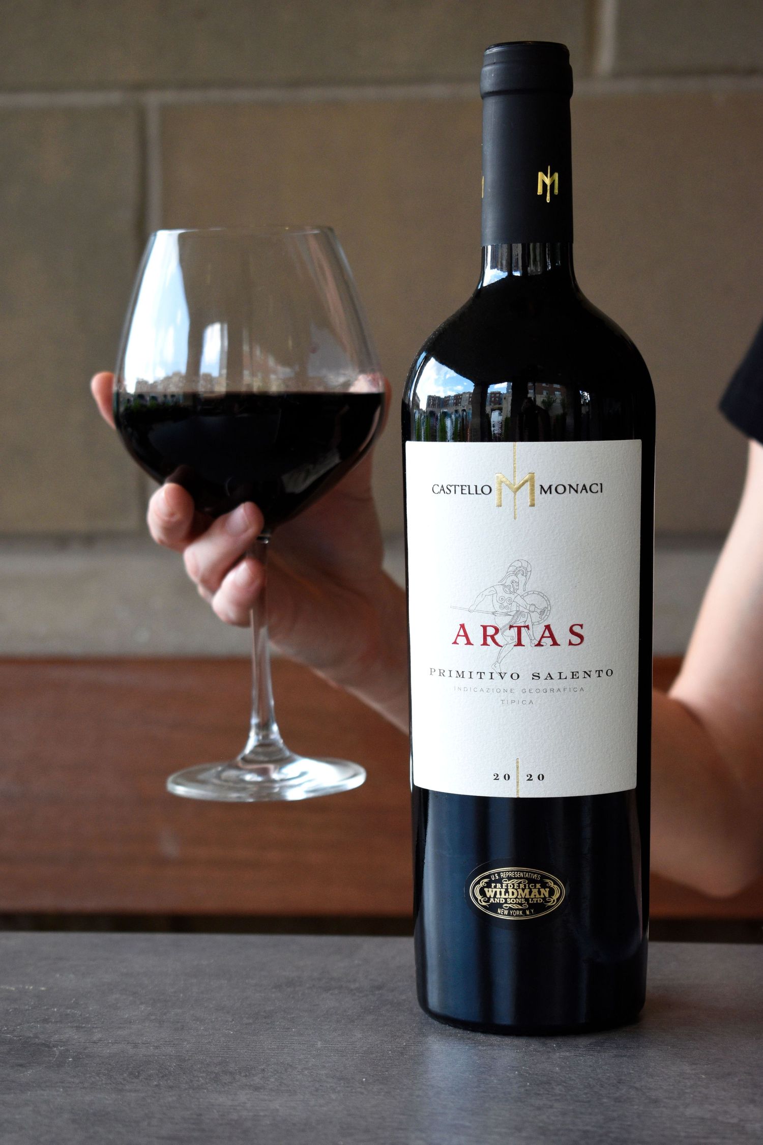 Castello Monaci Artas Primitivo Salento 2020 red wine bottle with a full glass held by hand.