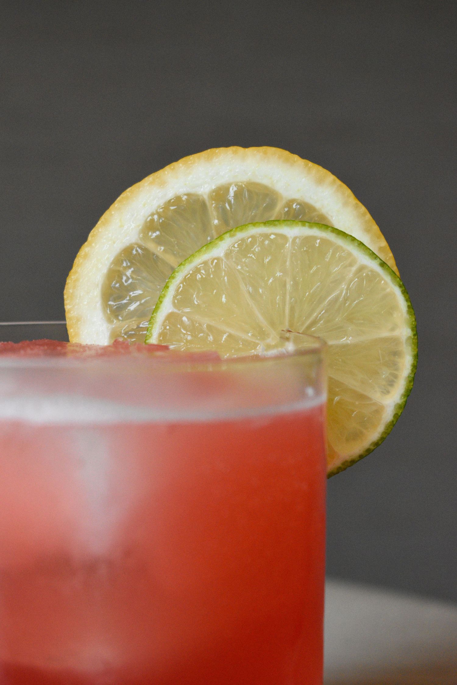 Close-up of a red cocktail garnished with overlapping lemon and lime slices on the rim of the glass.