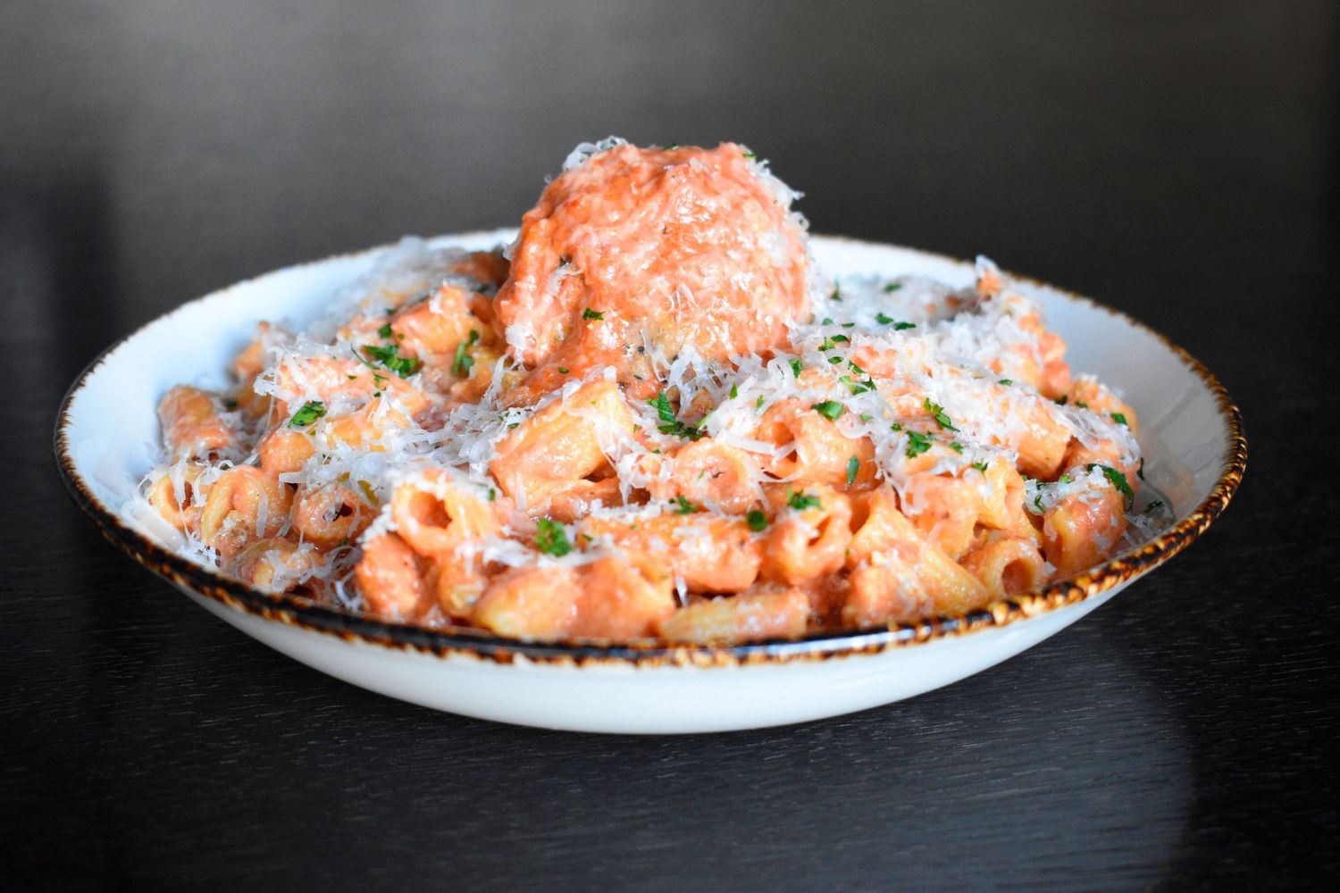 Creamy pasta dish topped with seasoned salmon and grated parmesan cheese served in a white bowl.