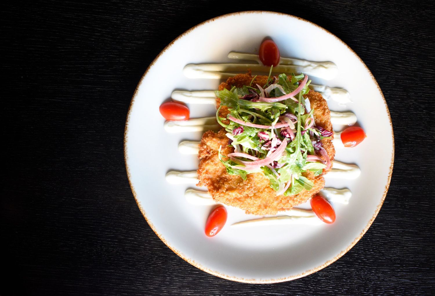 Overhead view of crispy crab cake with microgreens and red pepper sauce on a white plate.