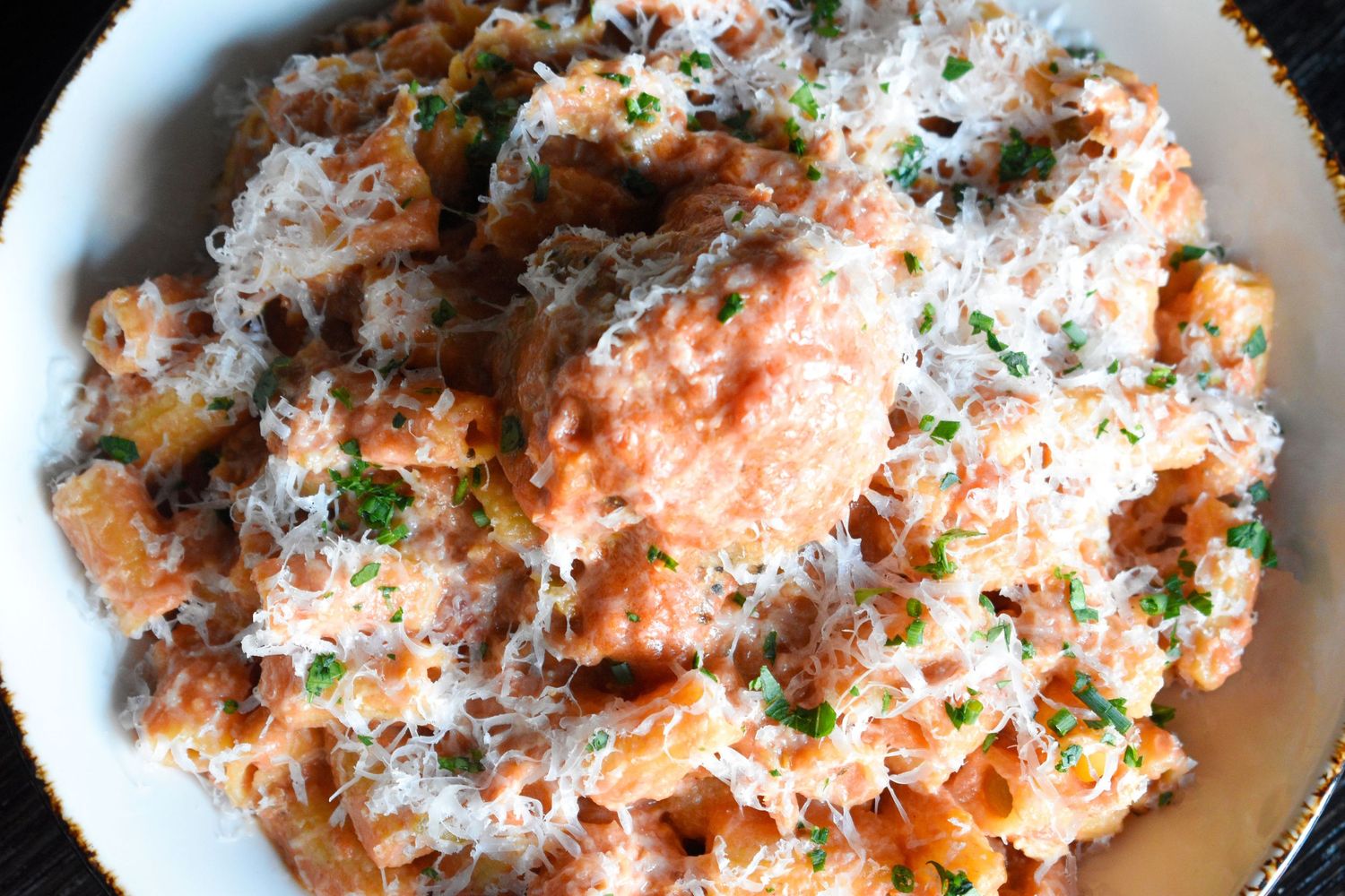 Close-up of creamy pasta with salmon, fresh herbs, and grated parmesan cheese in a white bowl.