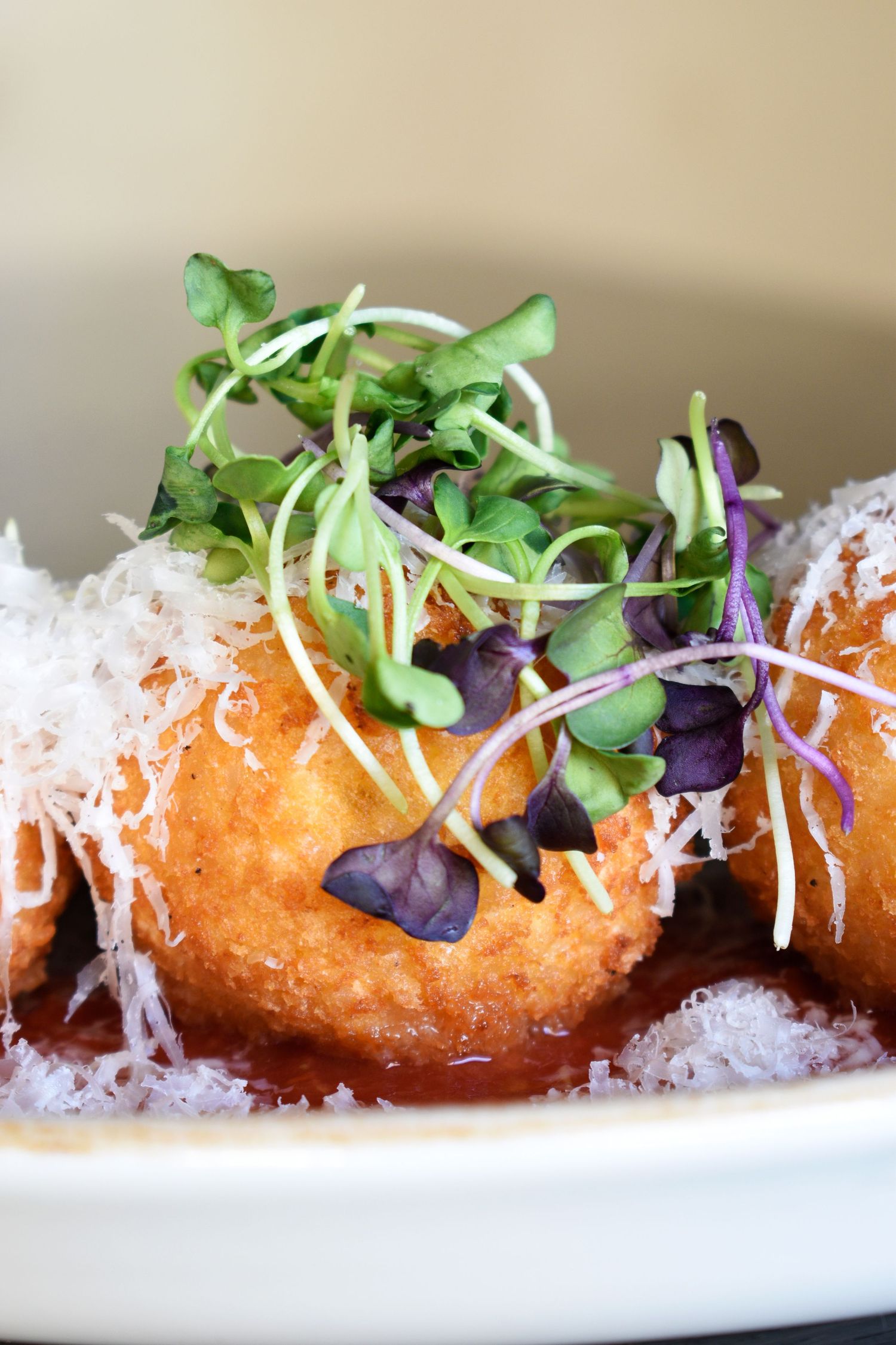 Close-up of golden fried arancini with tomato sauce, grated parmesan, and fresh mixed microgreens.