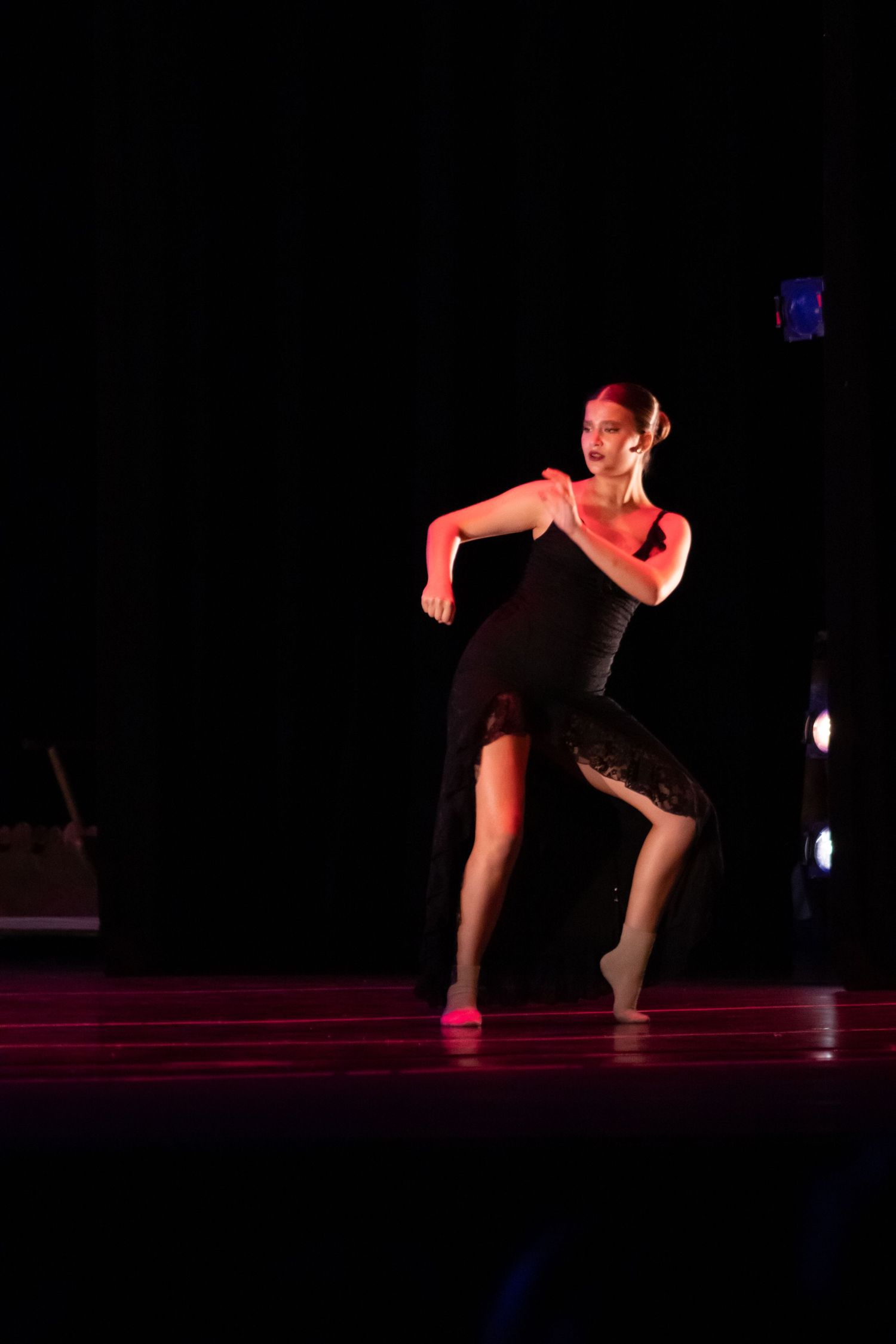 Female dancer in black dress performing contemporary dance under red stage lighting.