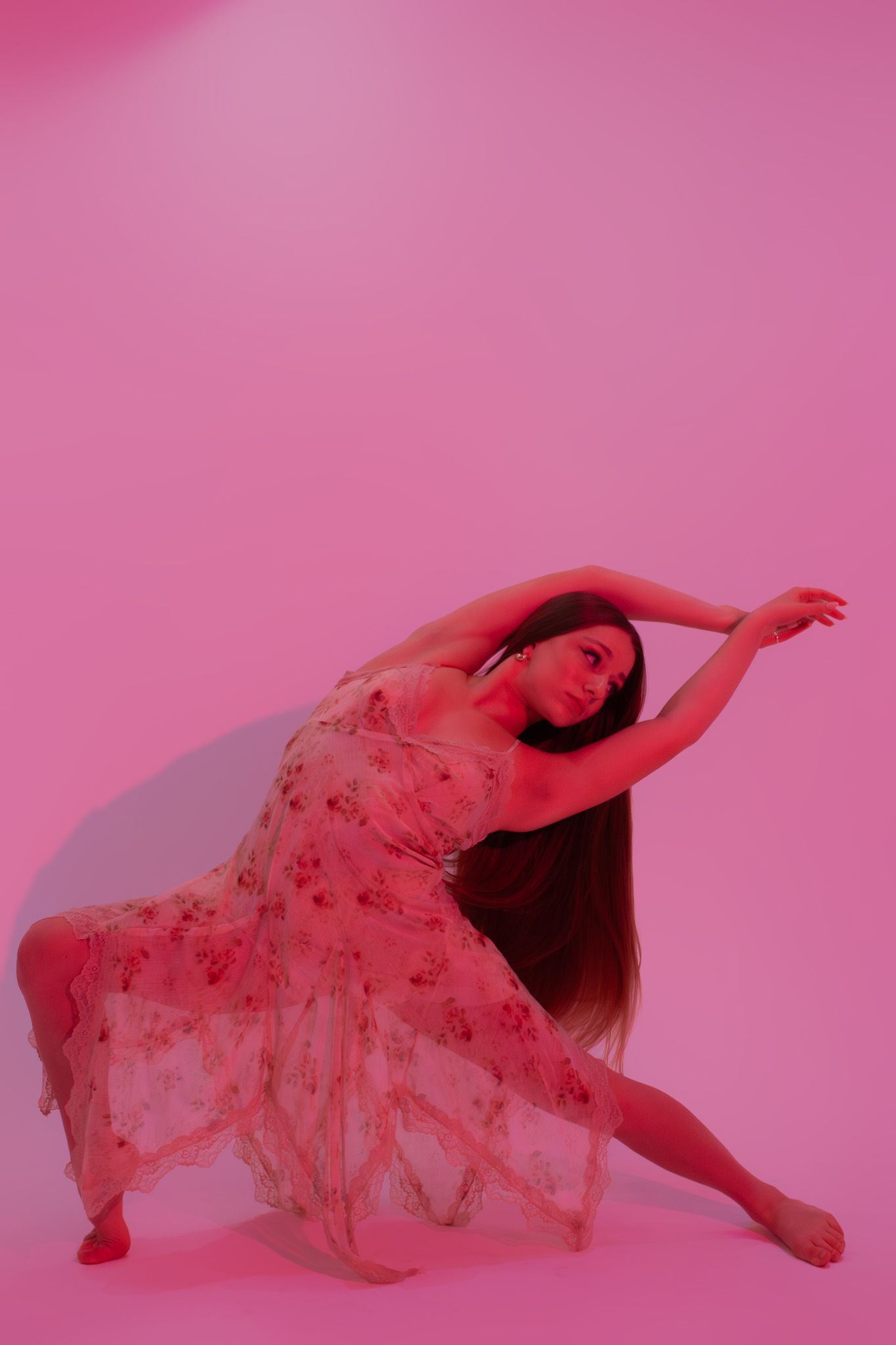 Dancer in floral dress posing gracefully on pink-lit studio floor.