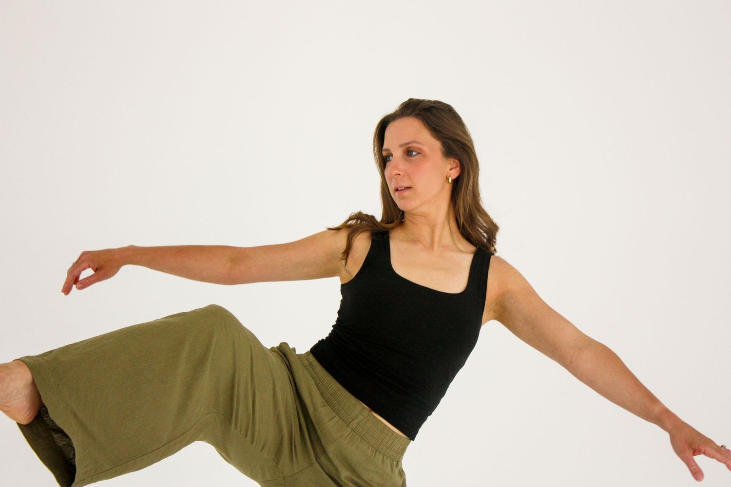 Female contemporary dancer in black top and olive pants performing an expressive movement pose.