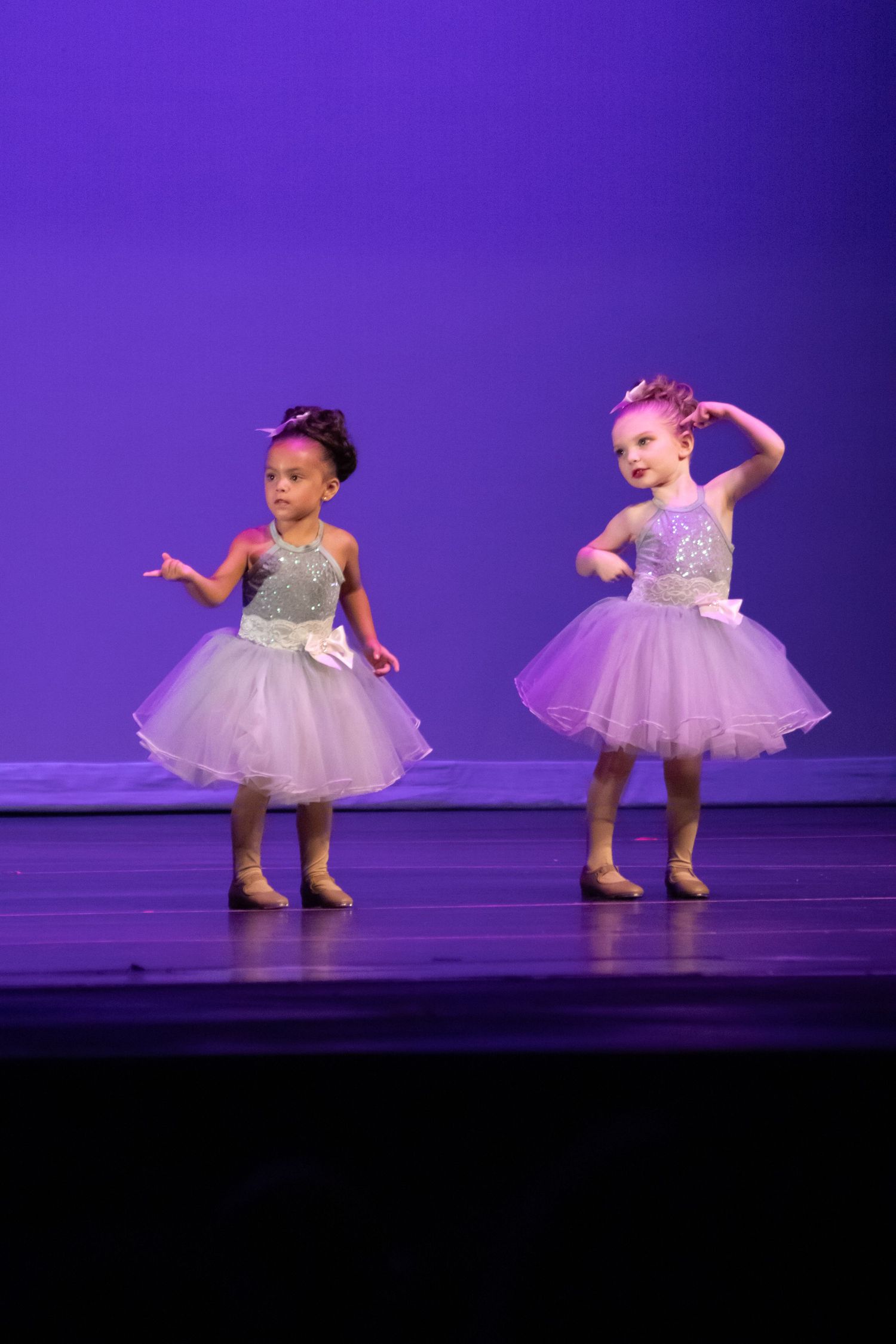 Two little girls in silver and lavender tutu dresses perform ballet on a purple-lit stage.