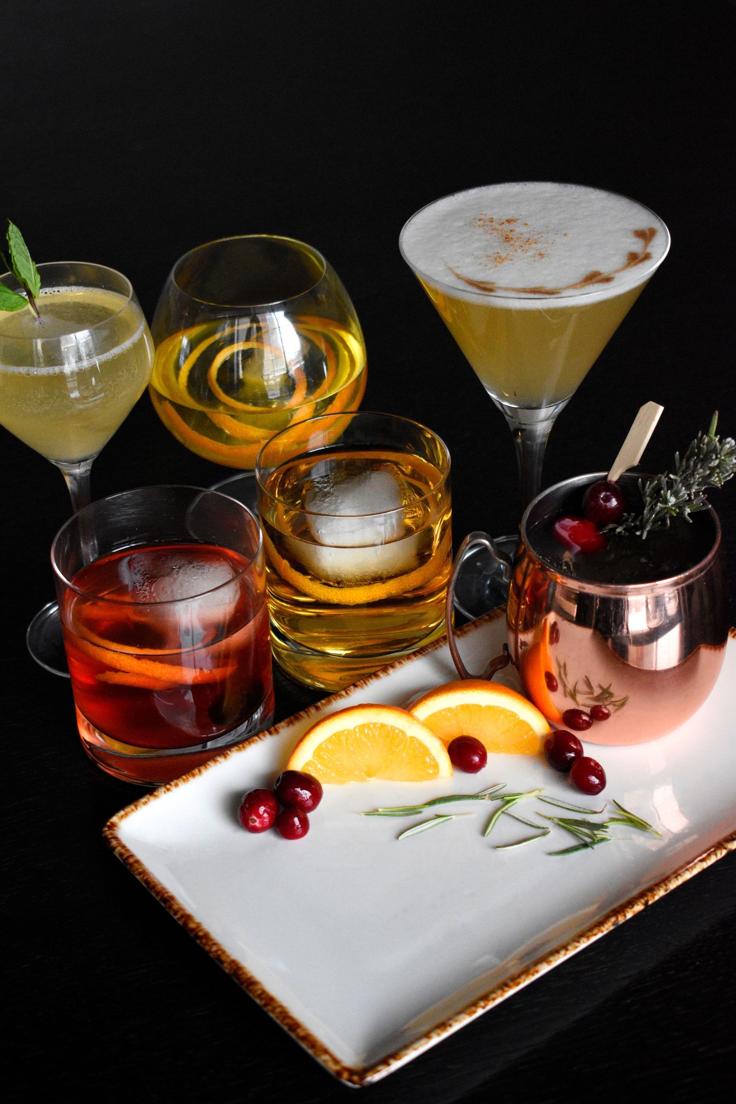 Collection of six elegant cocktails including martini, whiskey, and Moscow Mule on a tray.