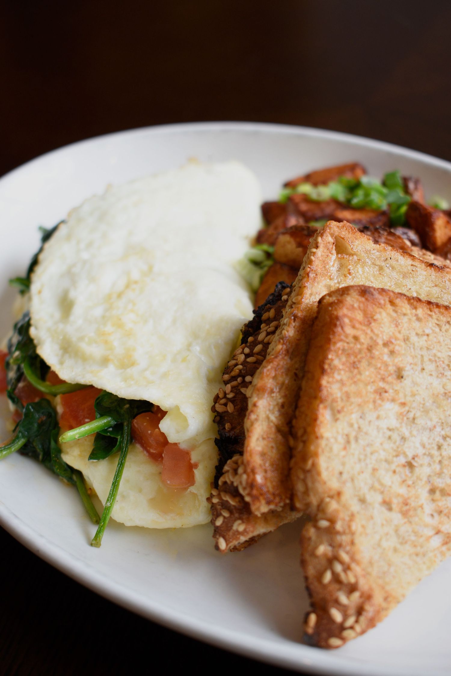 Breakfast plate with a fried egg over sauteed spinach and tomatoes served with multigrain toast slices.