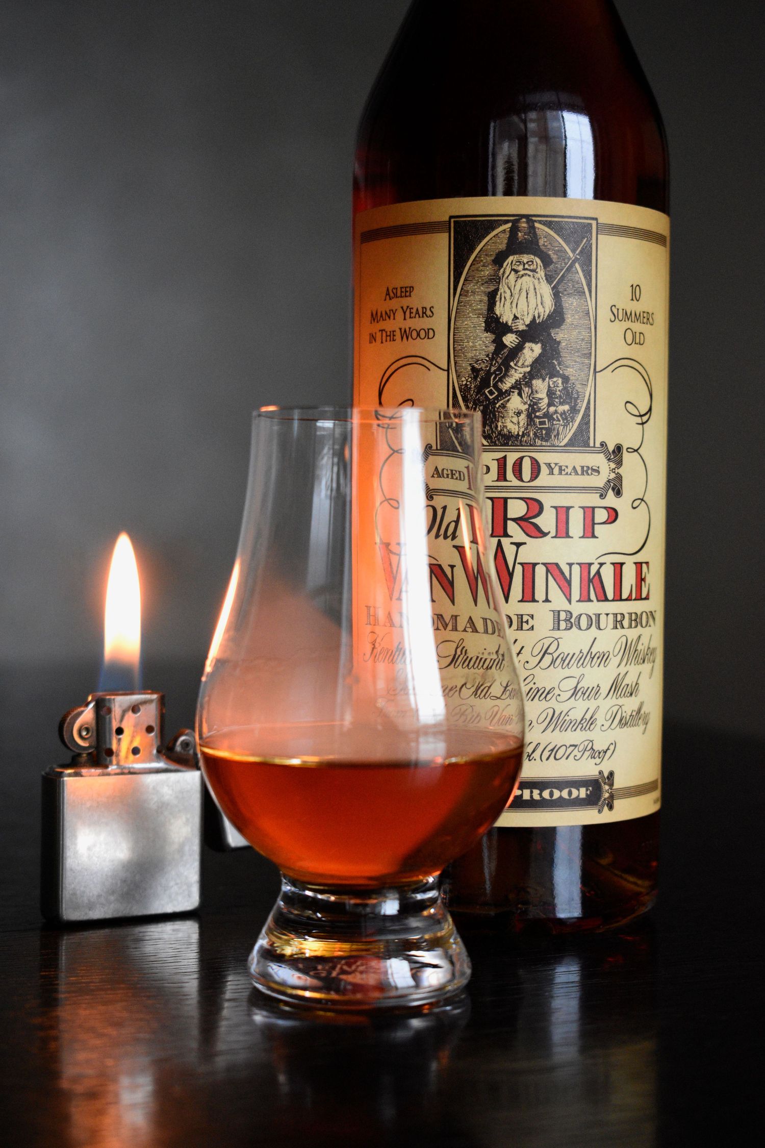 Old Rip Van Winkle 10-year bourbon bottle with Glencairn glass and lit Zippo lighter on dark surface.