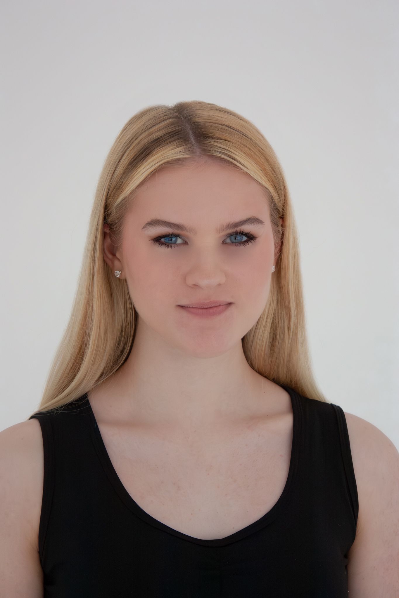 Young blonde woman with blue eyes wearing a black tank top poses against a white background.