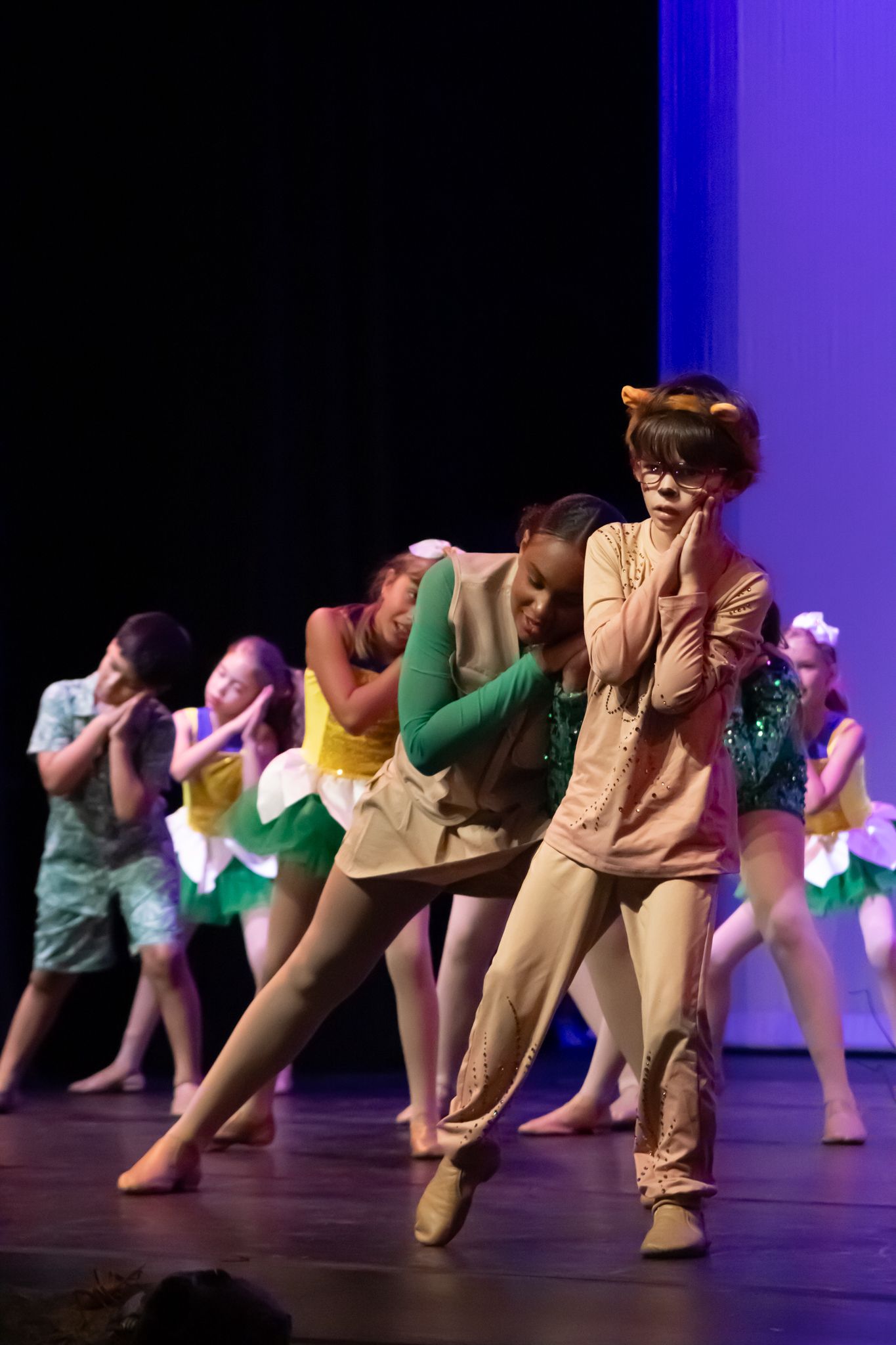 Young dancers in animal costumes perform an expressive group routine on a darkly lit stage.