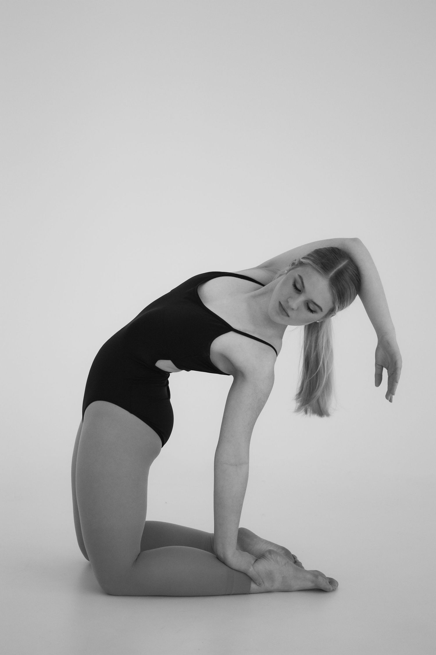 A female dancer in a black leotard kneels on the floor in a graceful pose in this black and white photo.