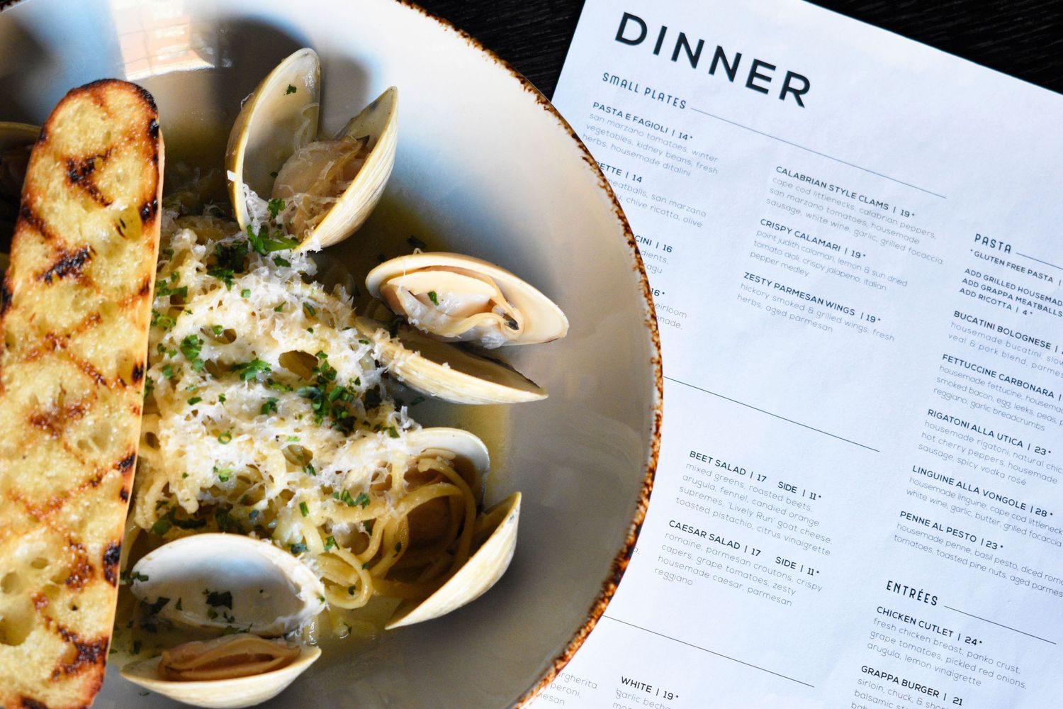 Linguine alle vongole with clams and grilled bread next to a Grappa restaurant dinner menu.