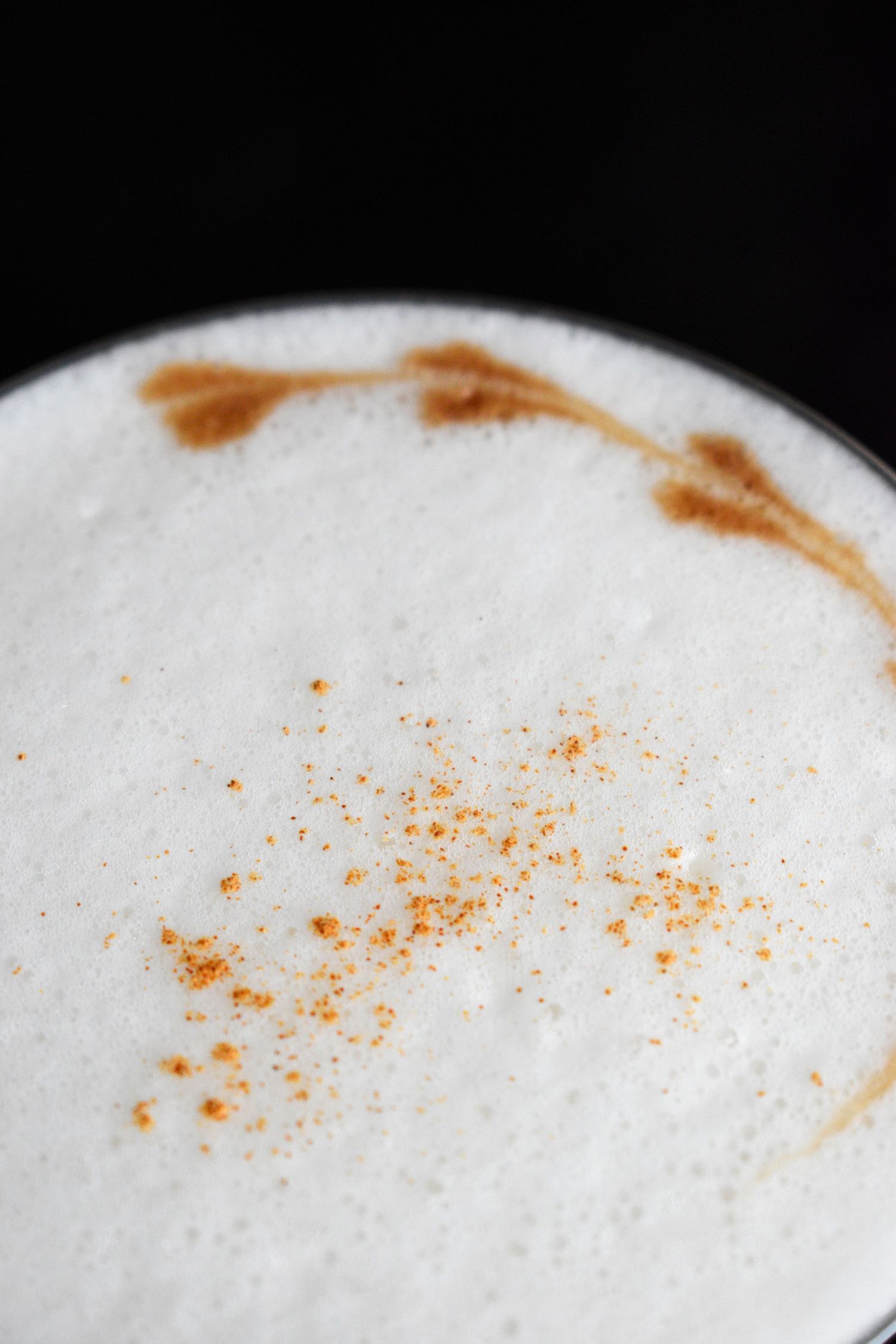 Close-up top view of a frothy cappuccino with cinnamon powder dusted on white foam.