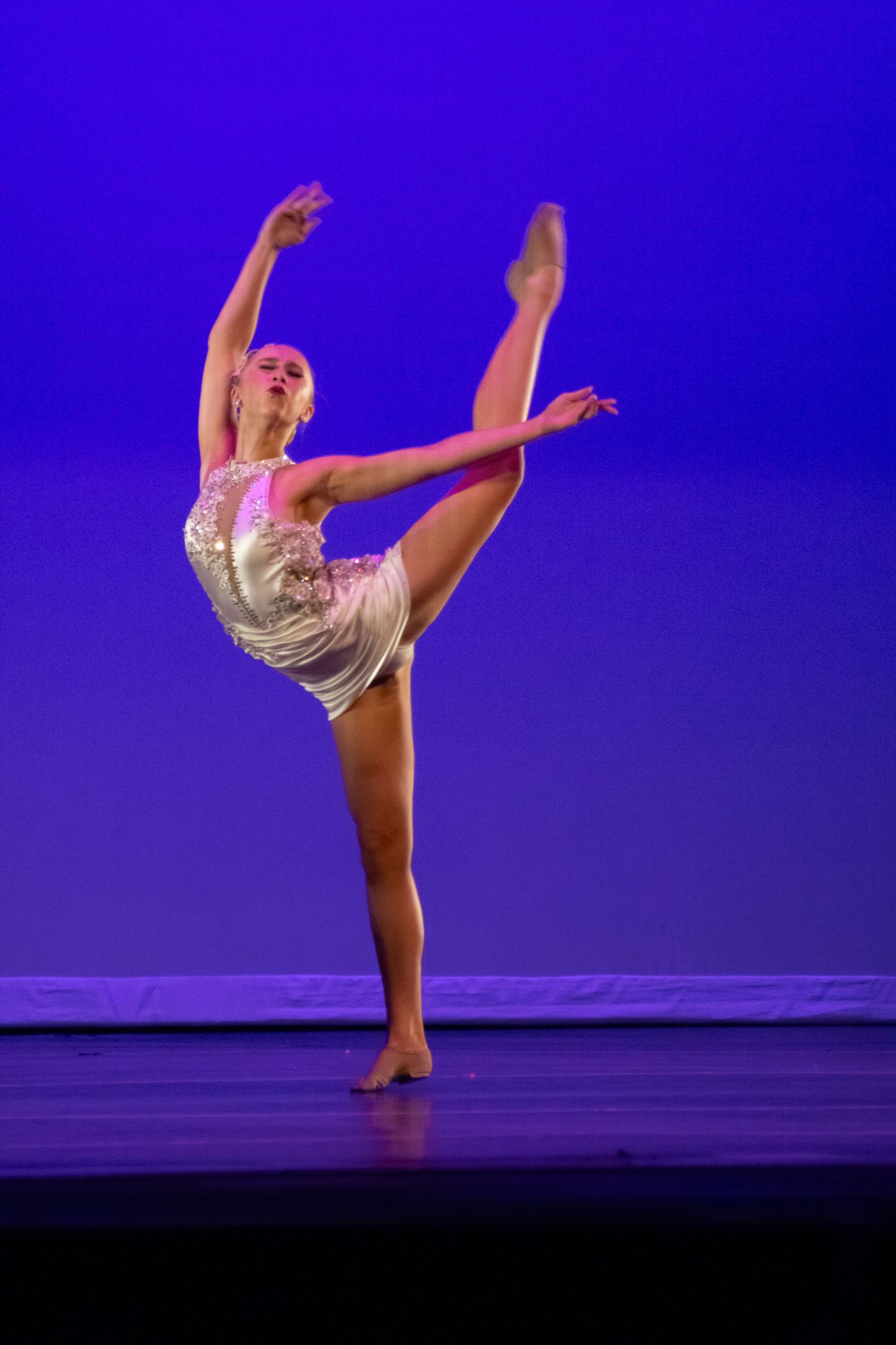 A dancer in a sparkly costume balances on one leg on stage.