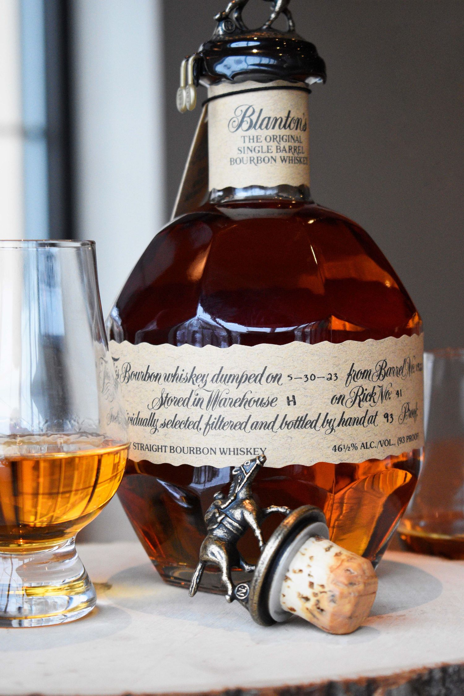 Blanton's Single Barrel Bourbon Whiskey bottle beside a Glencairn glass of whiskey on a natural wood surface.