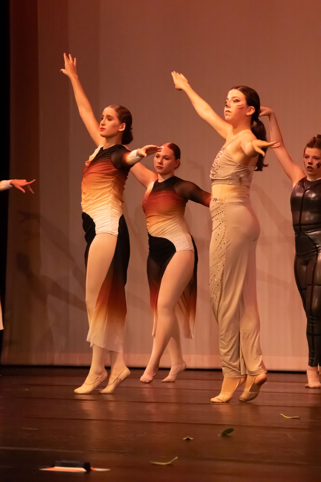 Young female dancers perform contemporary ballet on stage in gradient orange and black costumes.