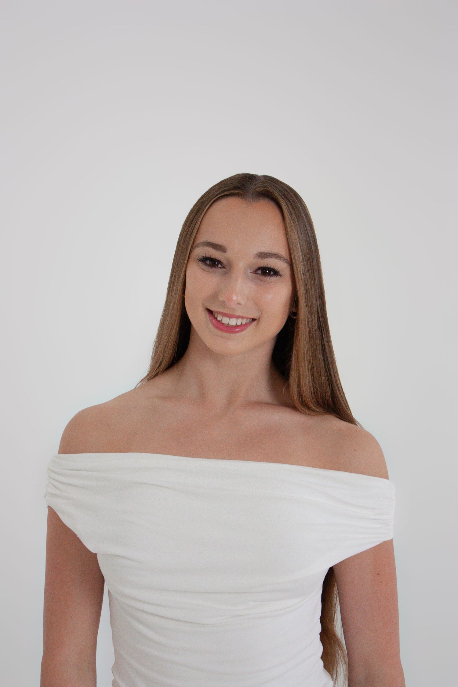 Young woman smiling in white off-shoulder dress against light background.