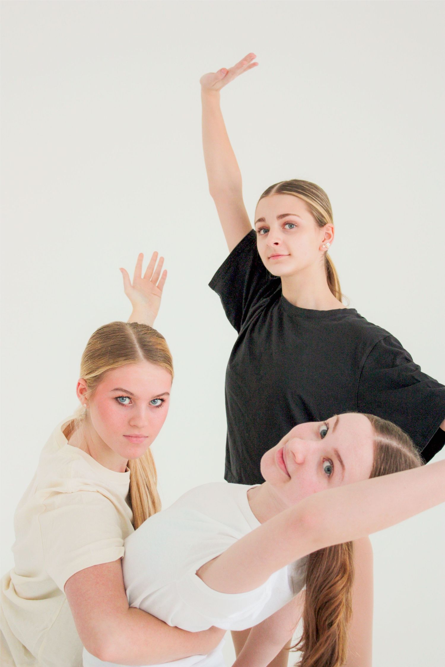 Three young female dancers in casual black and white tops pose together in a bright white studio.