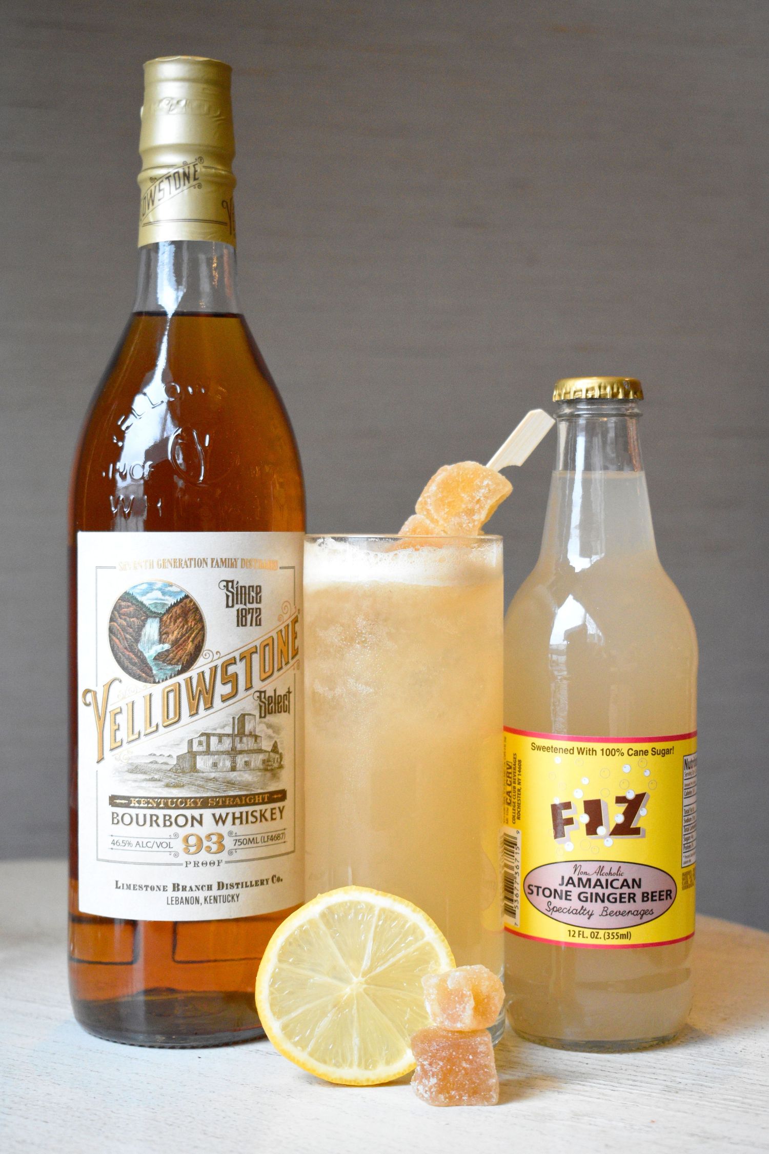 Yellowstone Bourbon Whiskey cocktail with FIZ Jamaican ginger beer, garnished with candied ginger and lemon slice.