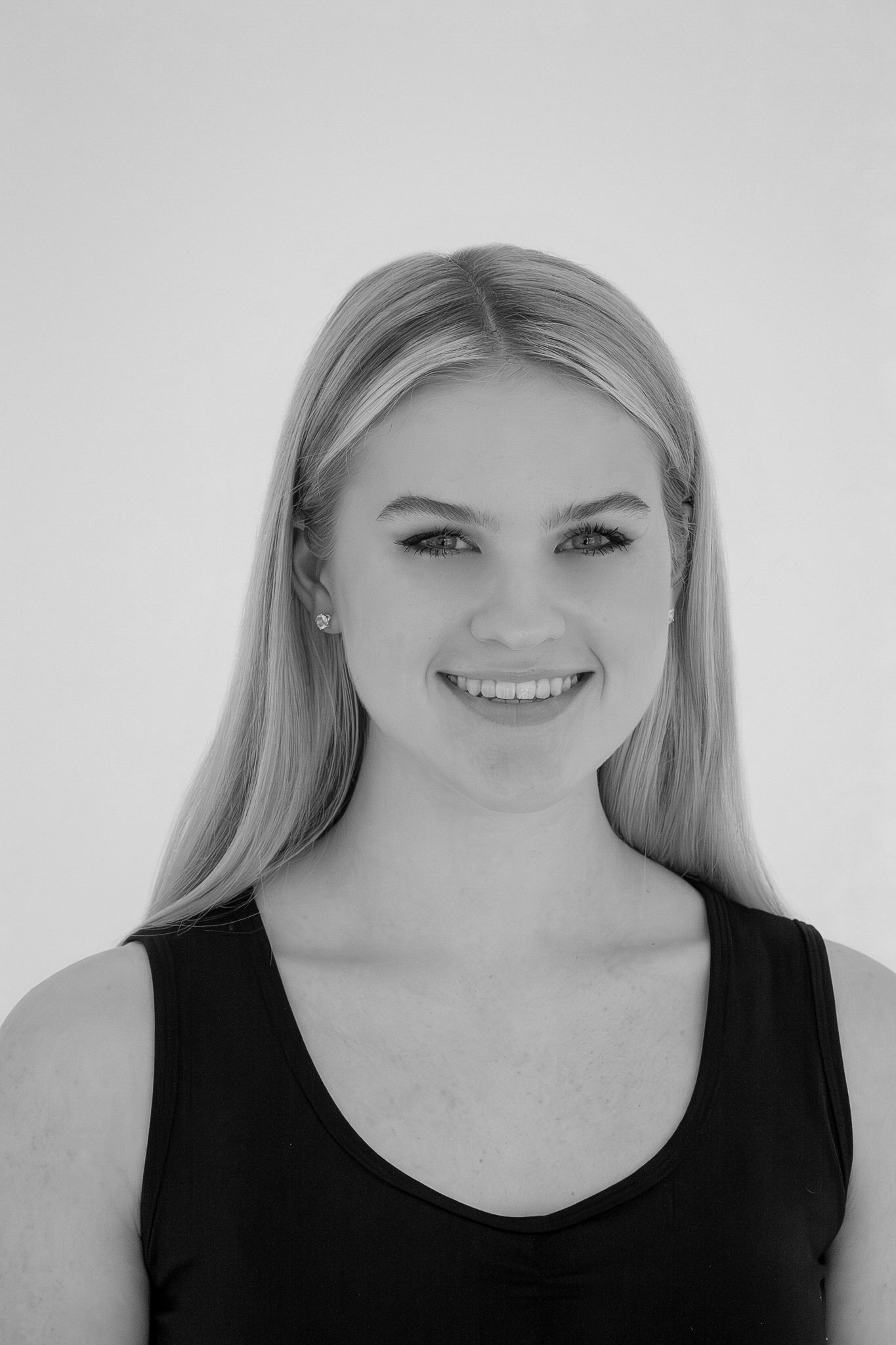Black and white portrait of smiling young blonde woman in black tank top on white background.