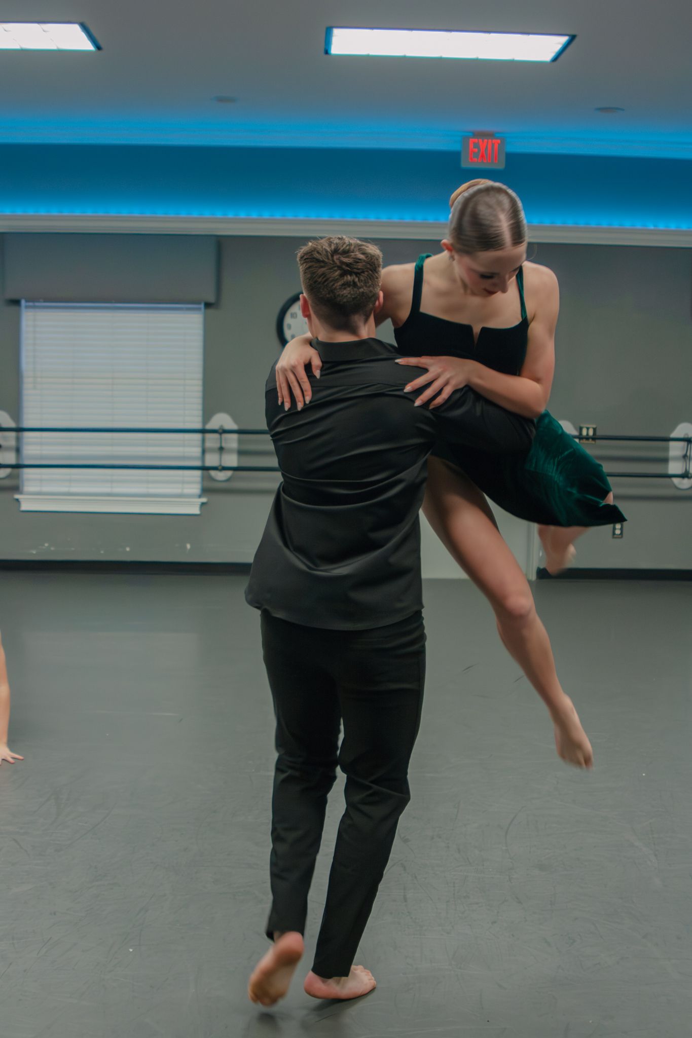 Male dancer lifts female ballet dancer in a black studio rehearsal.