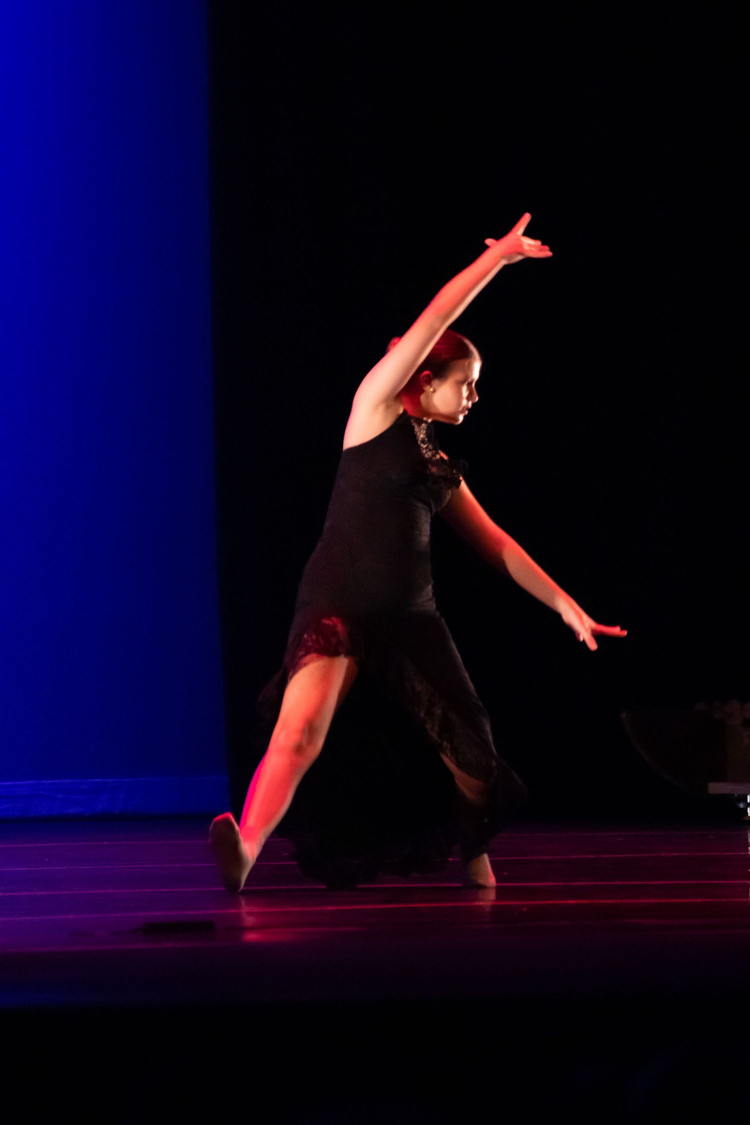 A dancer in a black dress performs an expressive contemporary routine under dramatic red and blue stage lighting.