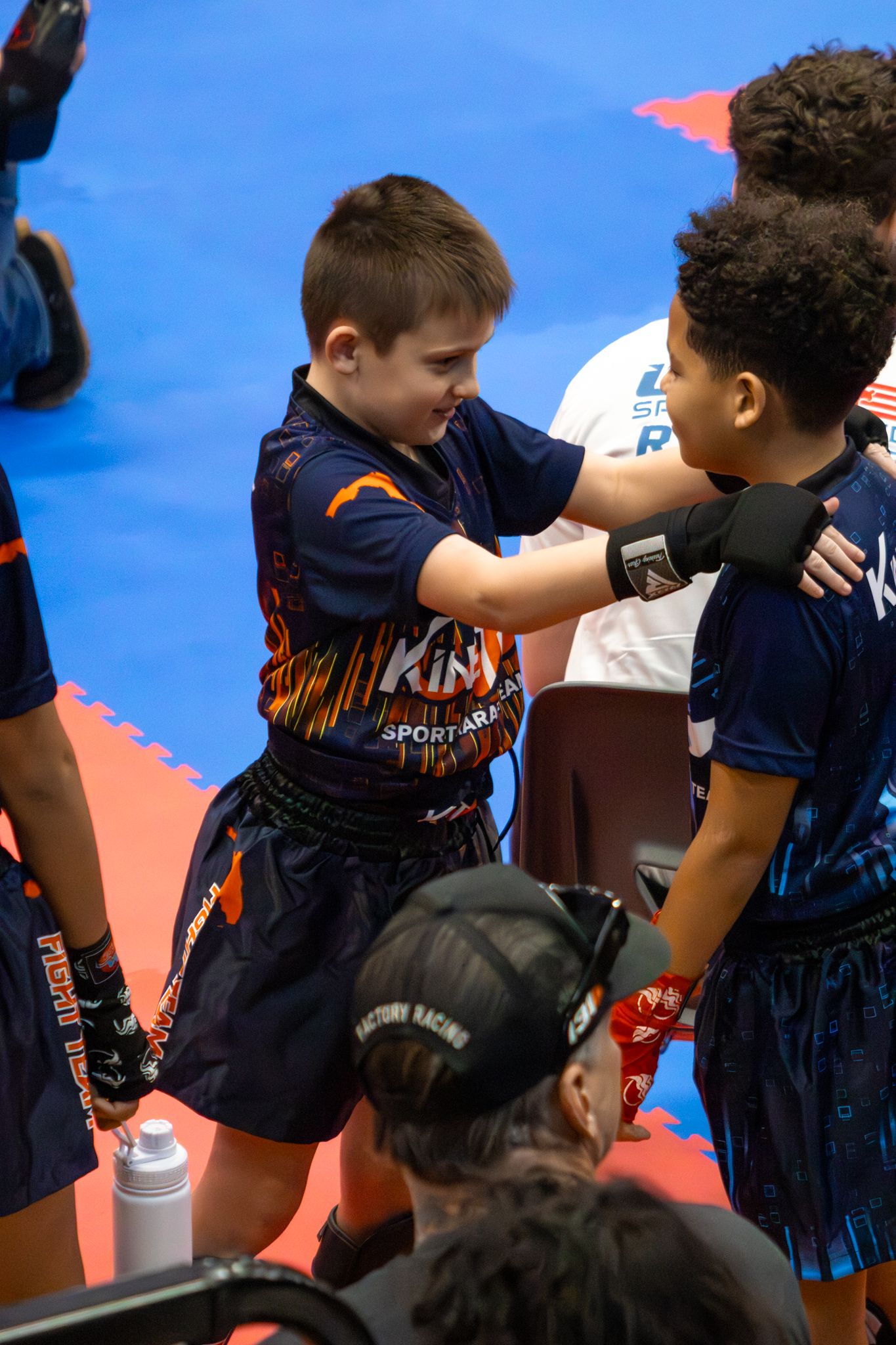 Two young boys in martial arts uniforms shake hands at a youth kickboxing competition.