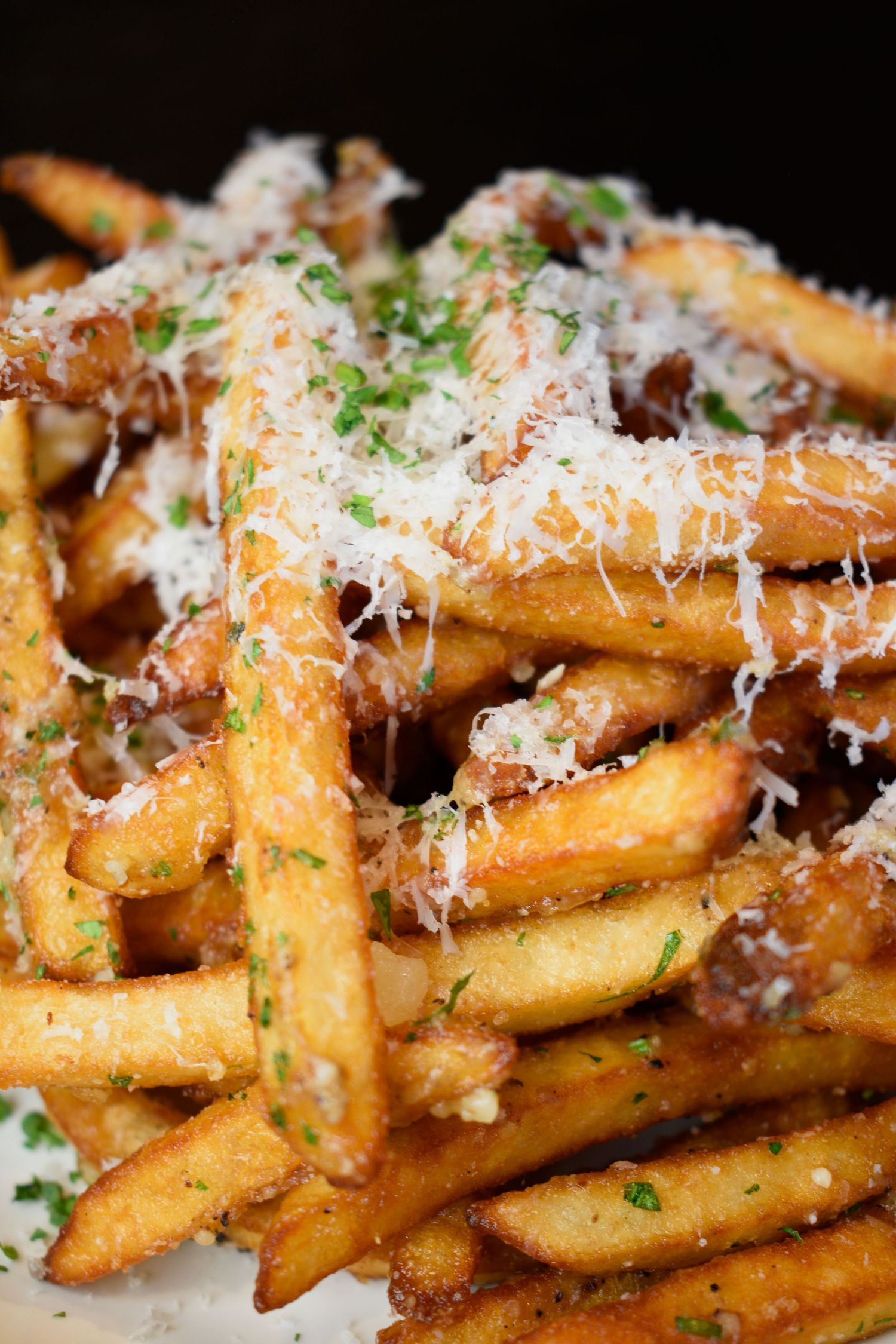 A close-up of crispy golden french fries topped with grated parmesan cheese and fresh chopped parsley.