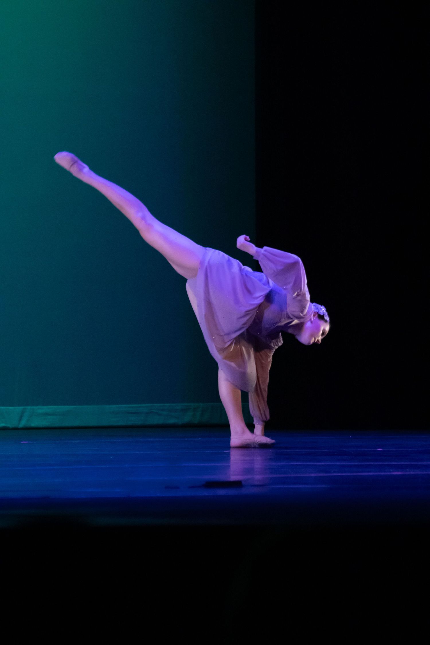 Dancer performs an impressive back arabesque in a white costume on a dark stage.