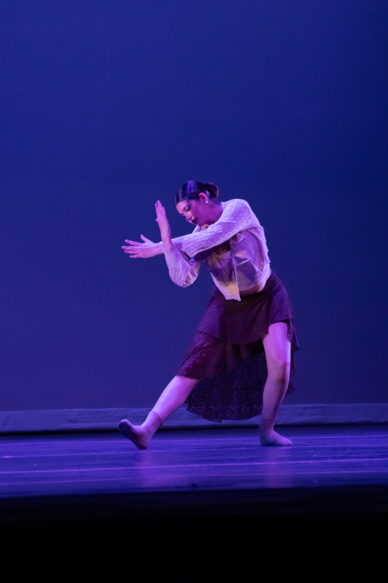 Female dancer in white top and burgundy skirt performs expressive contemporary dance on blue stage.