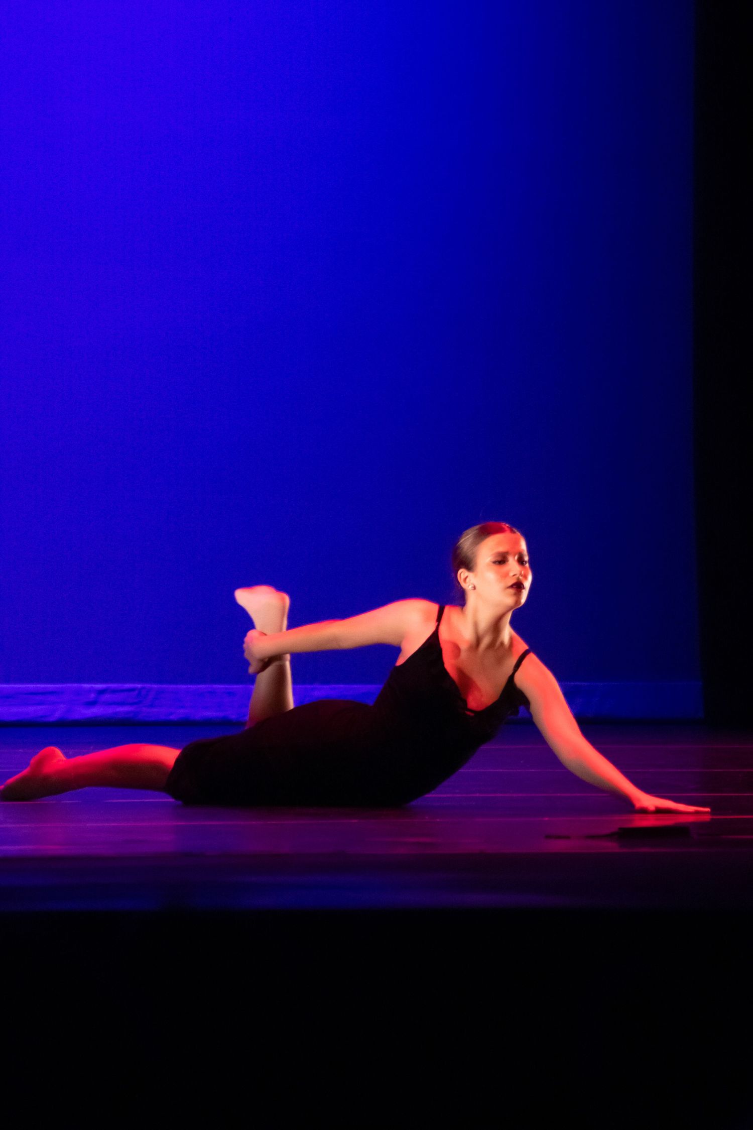 Female dancer in black performs a dramatic floor pose under blue and red stage lighting.