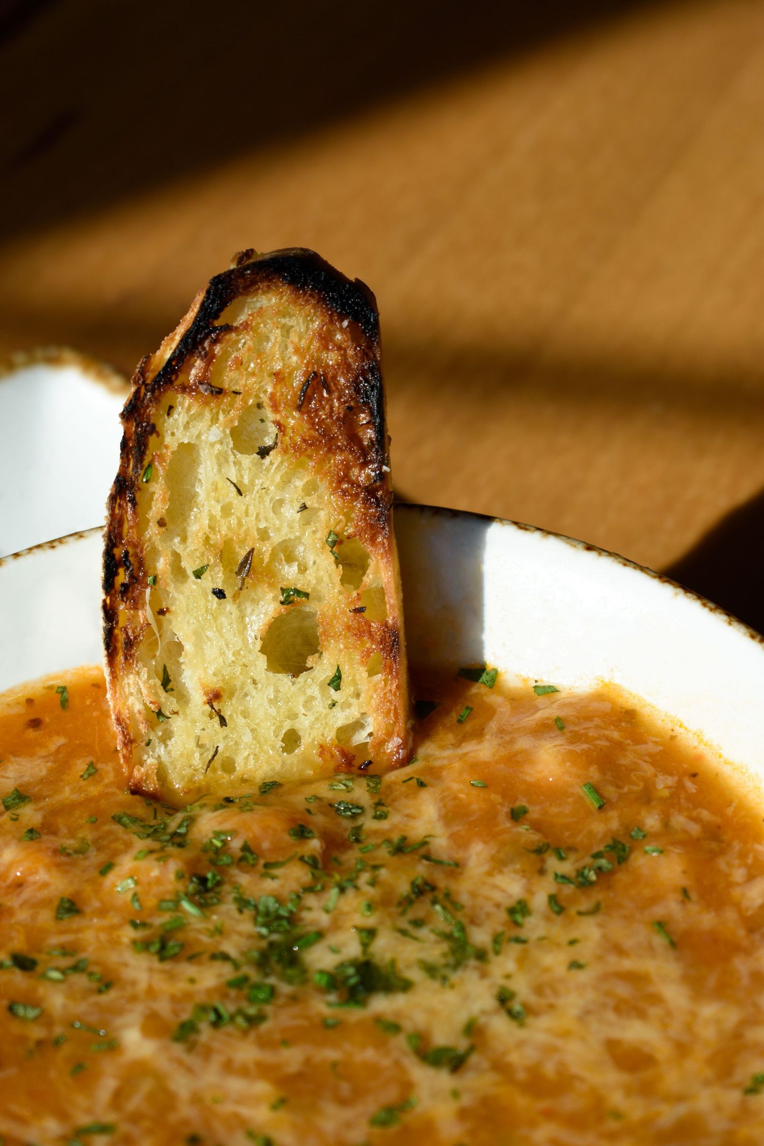 Close-up of a toasted bread crouton standing in a bowl of creamy herb-garnished tomato soup.