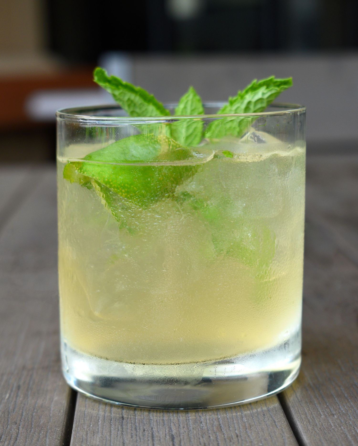 Refreshing cocktail with lime, mint leaves, and ice in a rocks glass on a wooden surface.