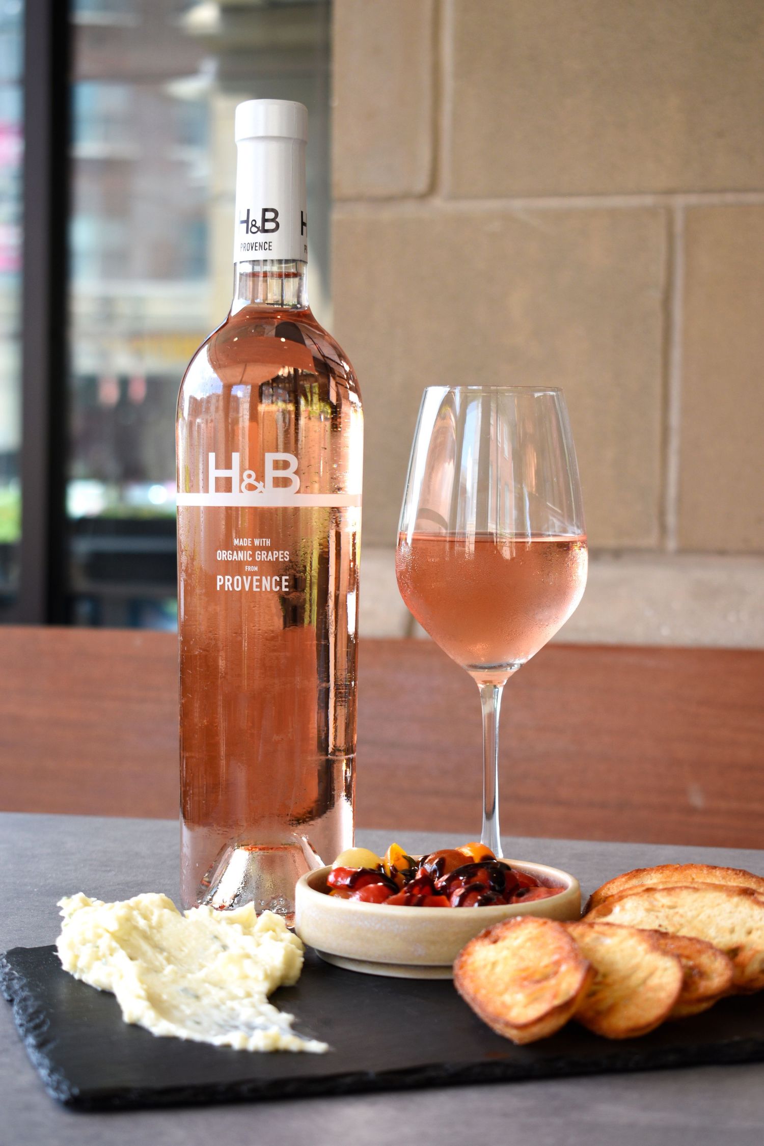 H&B Provence organic rosé wine bottle with poured glass and slate board with bruschetta and cheese.