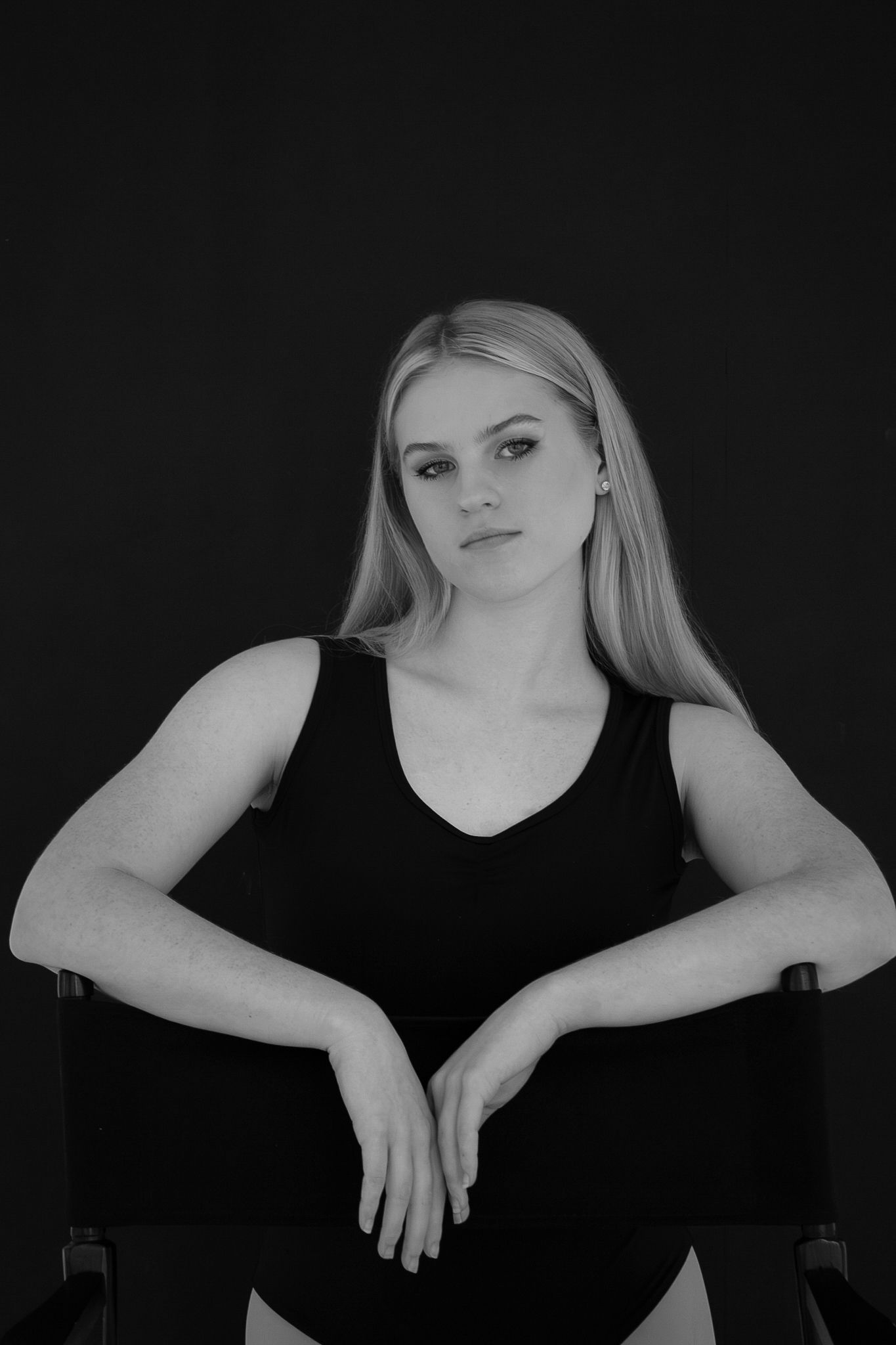Black and white portrait of a blonde woman in a black tank leotard seated in a director's chair.