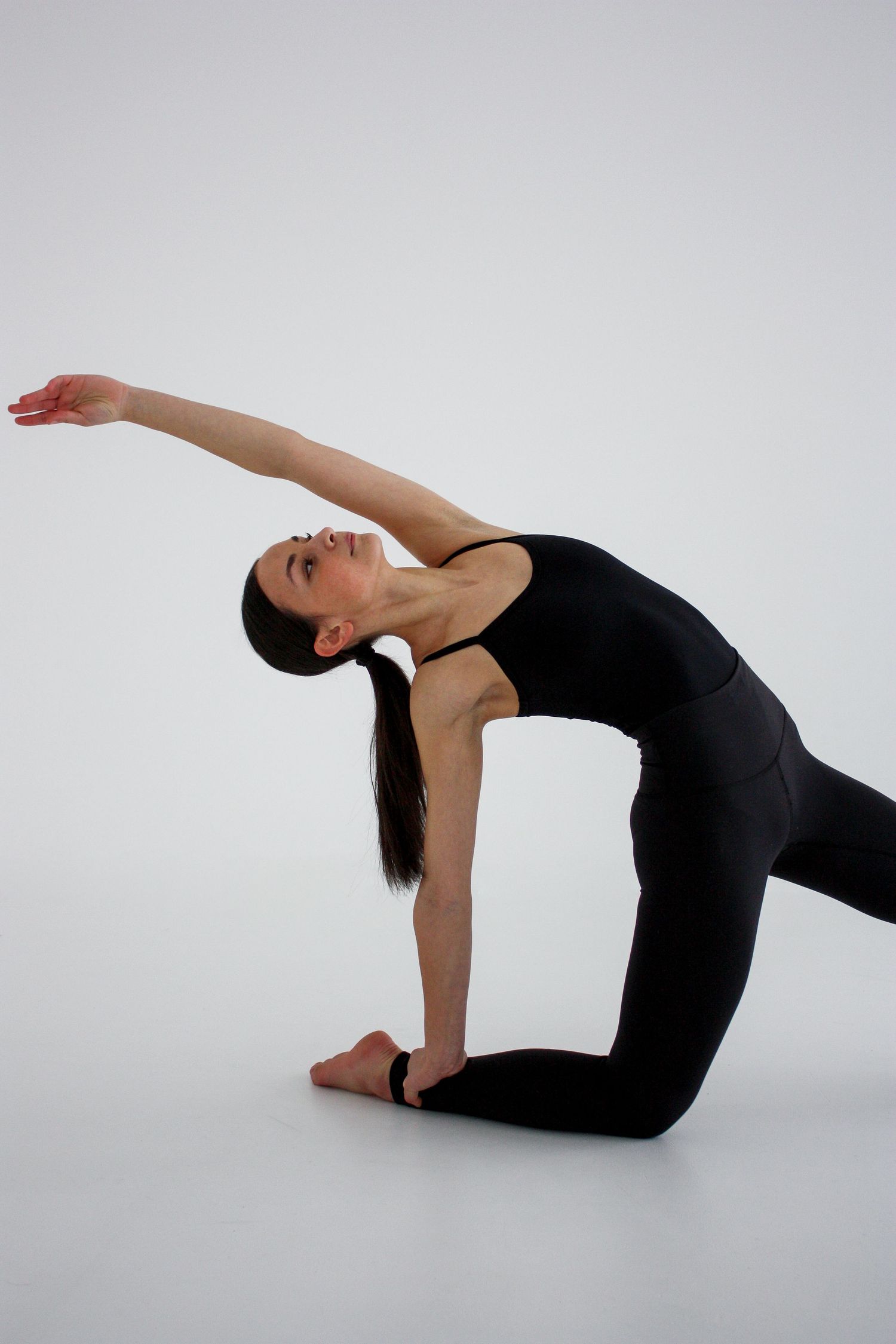 Dancer in black performs graceful side stretch with arm raised in white studio.