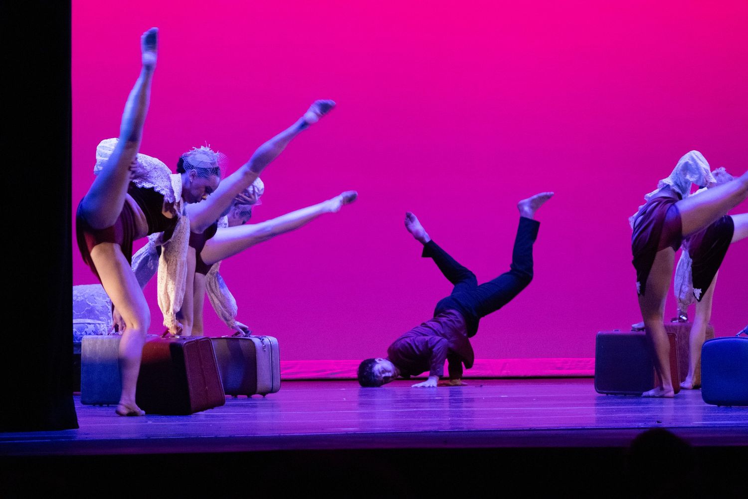 A group of dancers perform acrobatic moves on a pink-lit stage with decorative props.