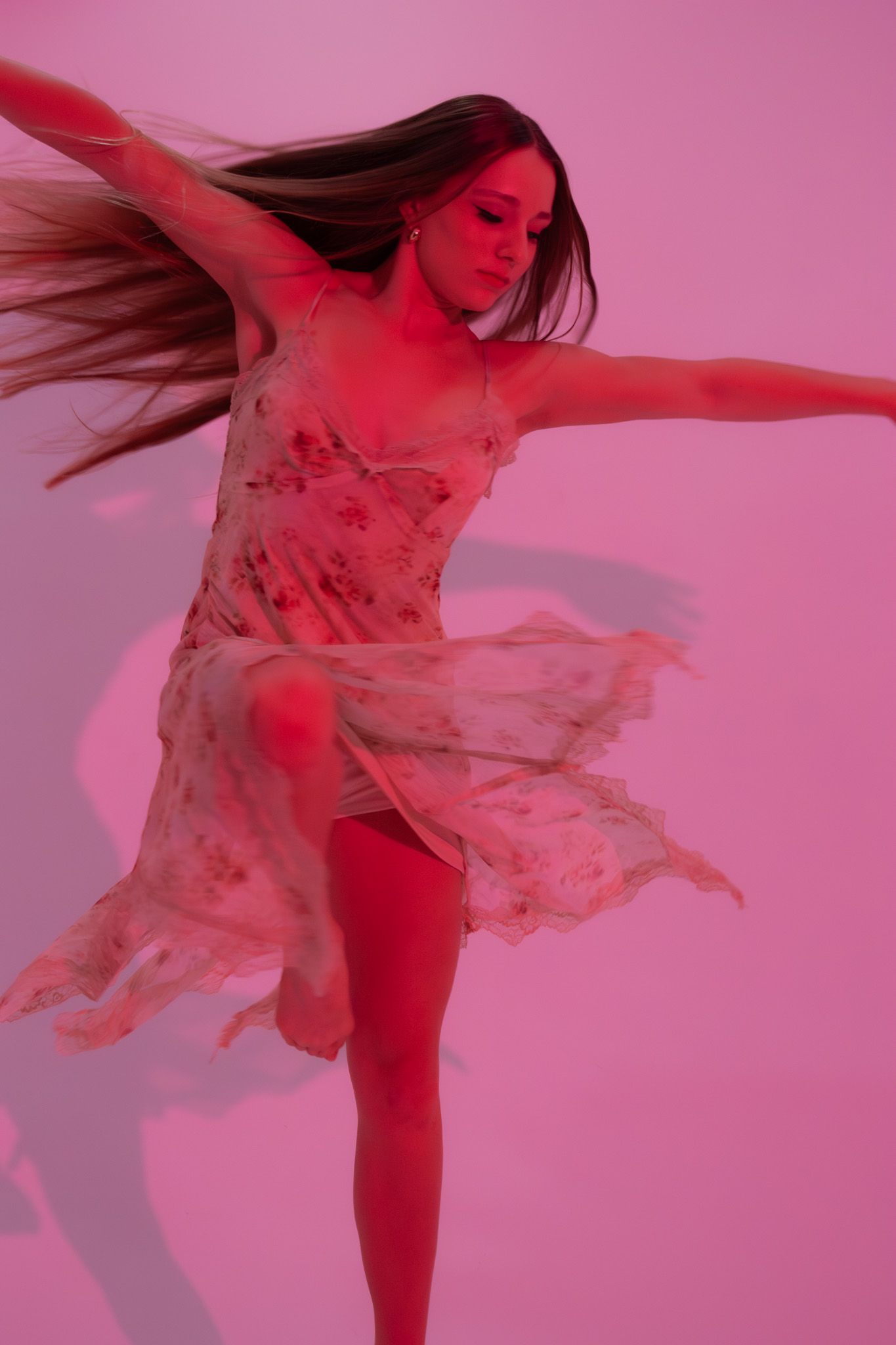 Young dancer in floral slip dress spins with flowing hair under pink studio lighting.