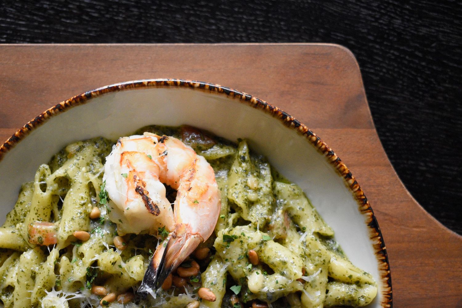 Pesto penne pasta topped with a grilled shrimp and parmesan in a rustic ceramic bowl.