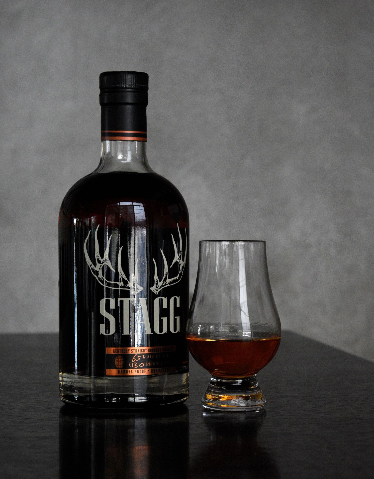 Stagg barrel proof straight bourbon whiskey bottle beside a Glencairn glass on a dark surface.