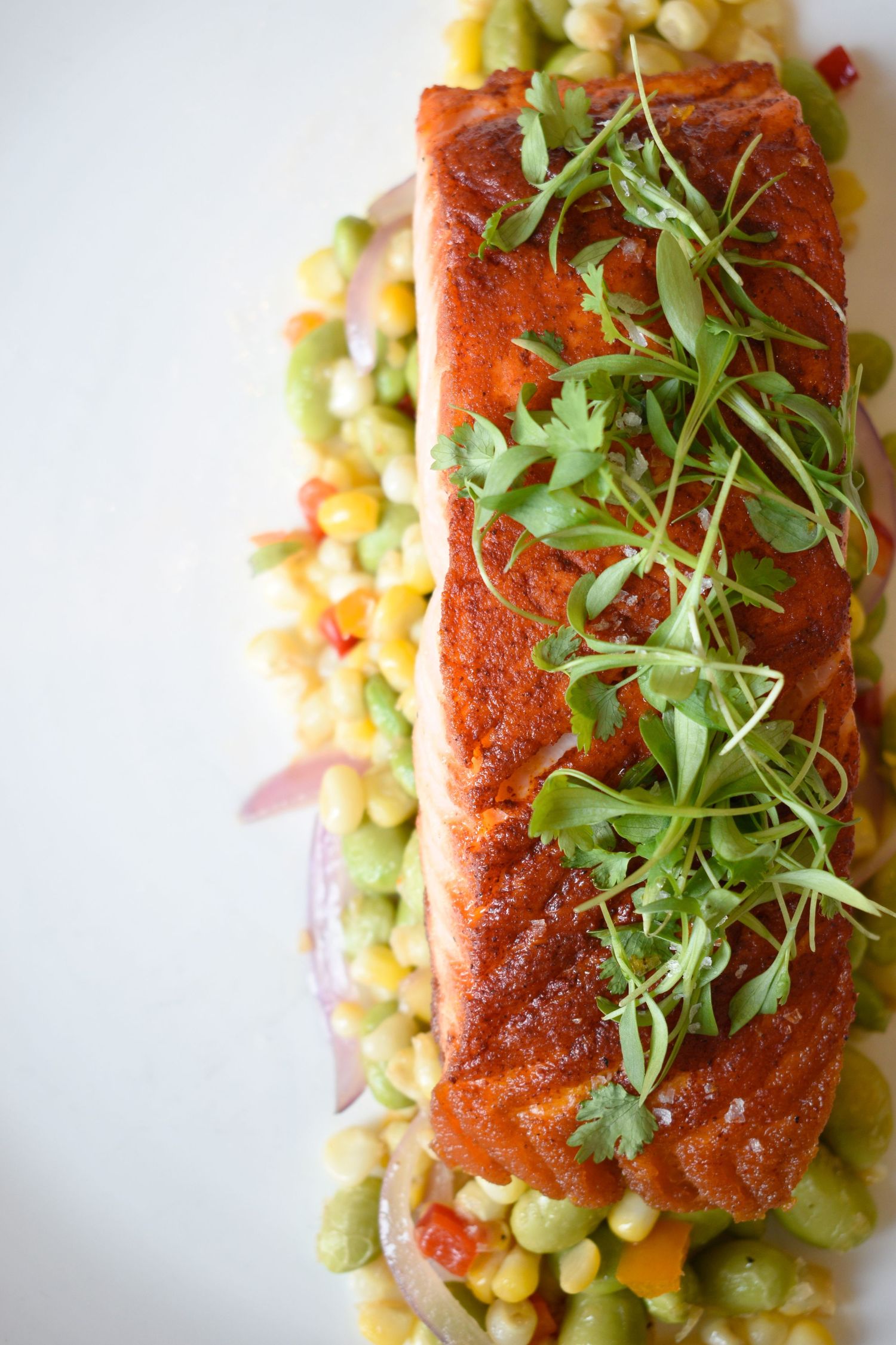 Top-down view of pan-seared salmon fillet topped with fresh microgreens on a corn and edamame succotash.
