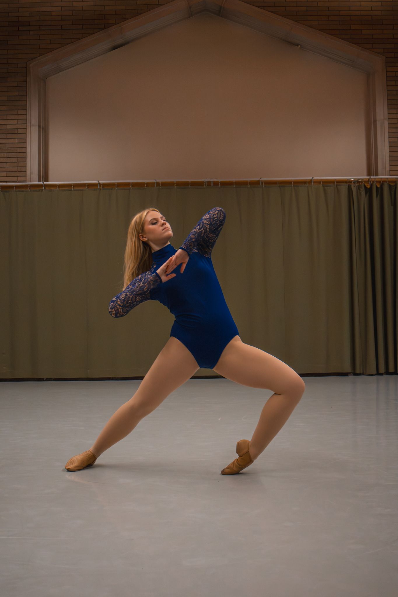 Blonde dancer in blue leotard performing an elegant lunge pose in a dance studio.