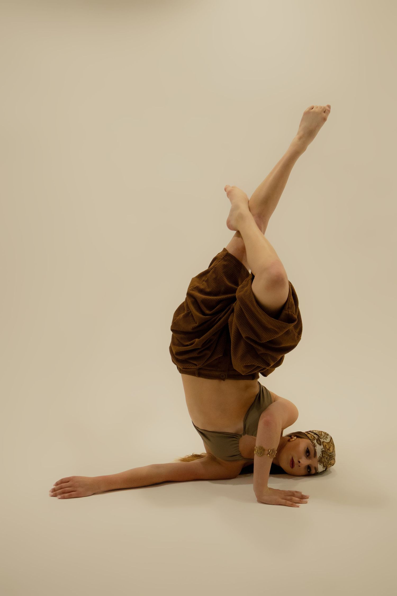 Flexible dancer performs advanced inverted pose with legs raised on a neutral beige studio background.