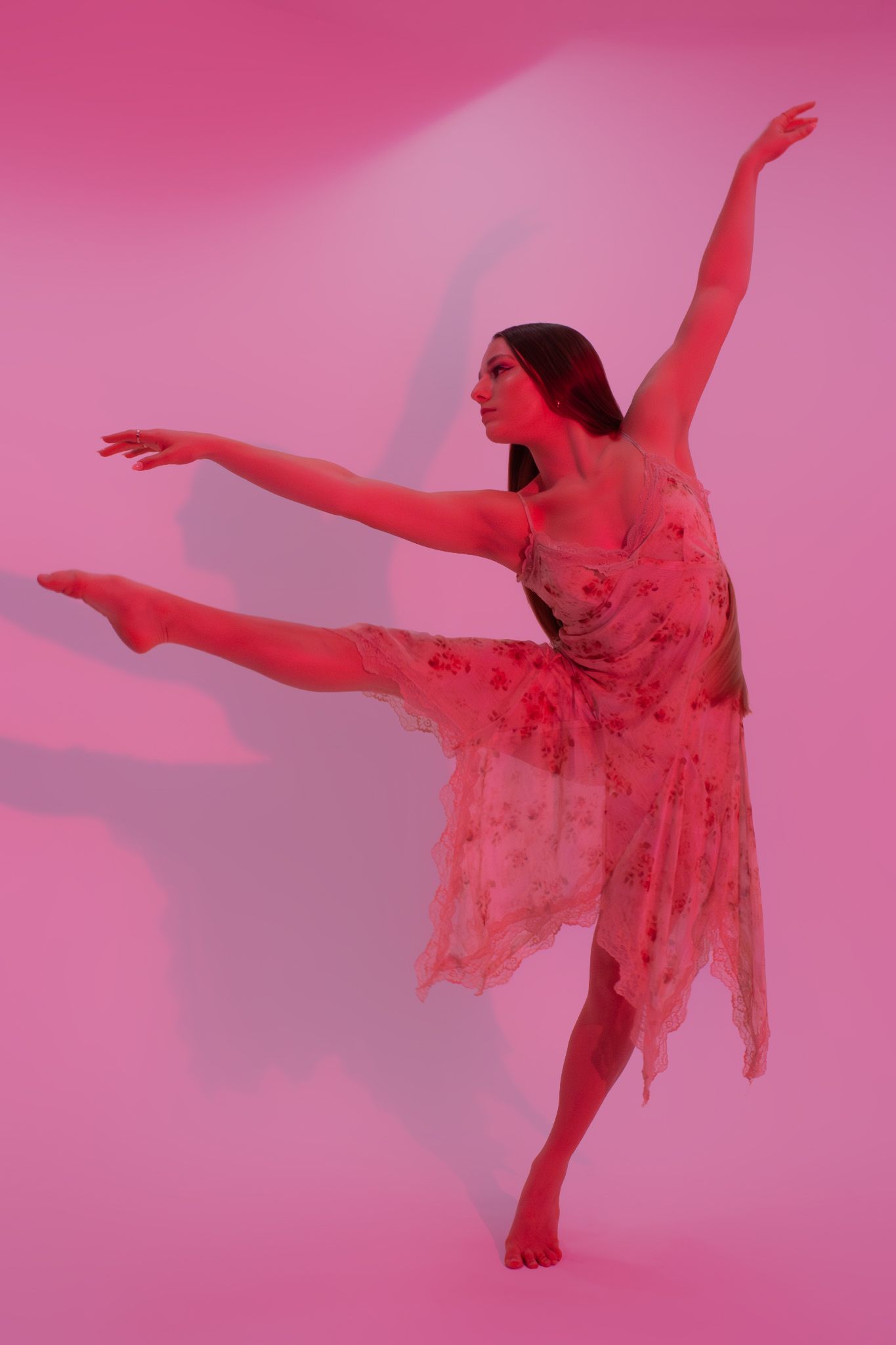 Graceful ballet dancer in floral dress performing arabesque on pink background.