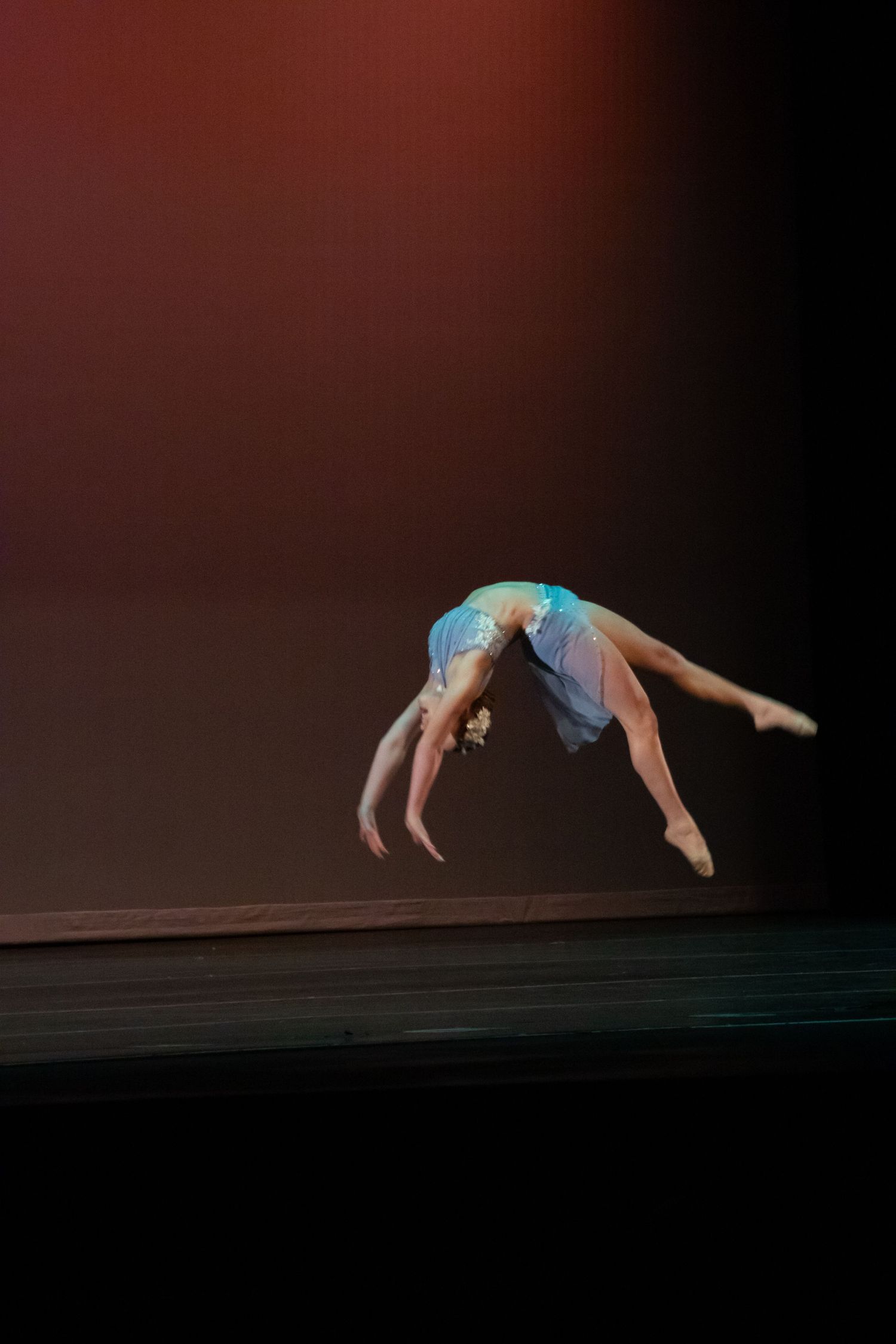 Gymnast in blue leotard executes a stunning back aerial flip on a dark stage.