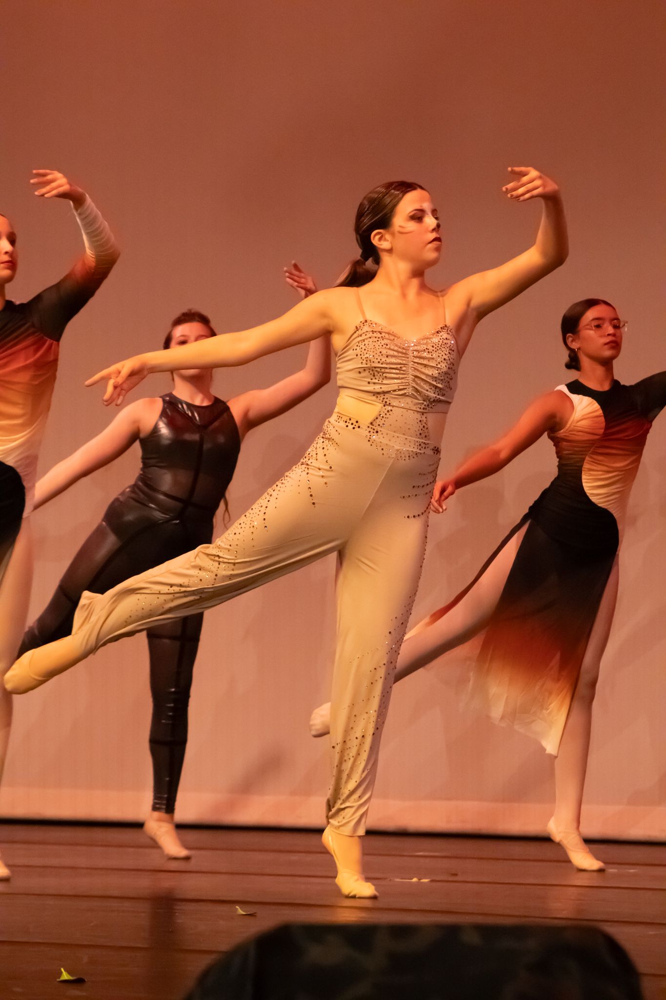 Elegant dancers perform contemporary ballet on stage, with the lead dancer in a beaded costume balancing on one leg.