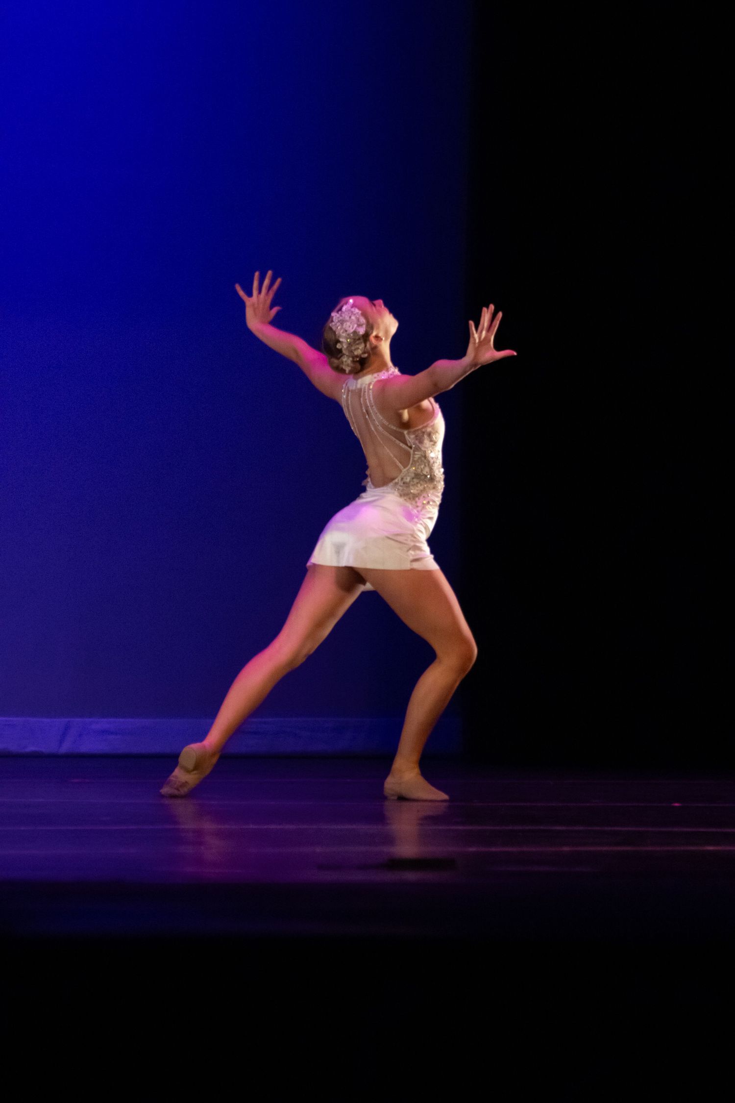 A female dancer in a white costume performs an expressive contemporary routine under warm stage lights.