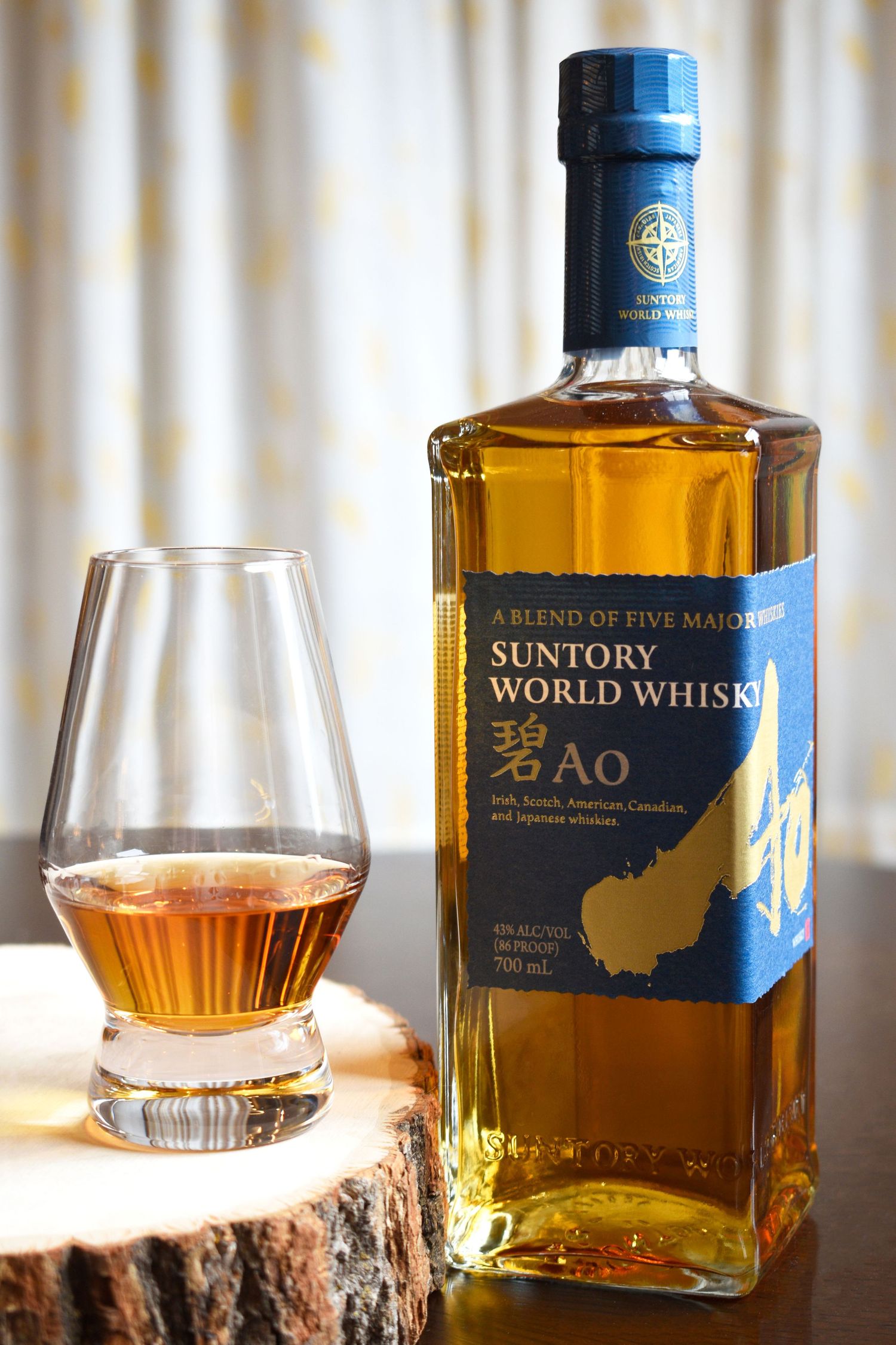 Suntory World Whisky Ao blend of five major whiskies bottle with a Glencairn glass on a wooden coaster.
